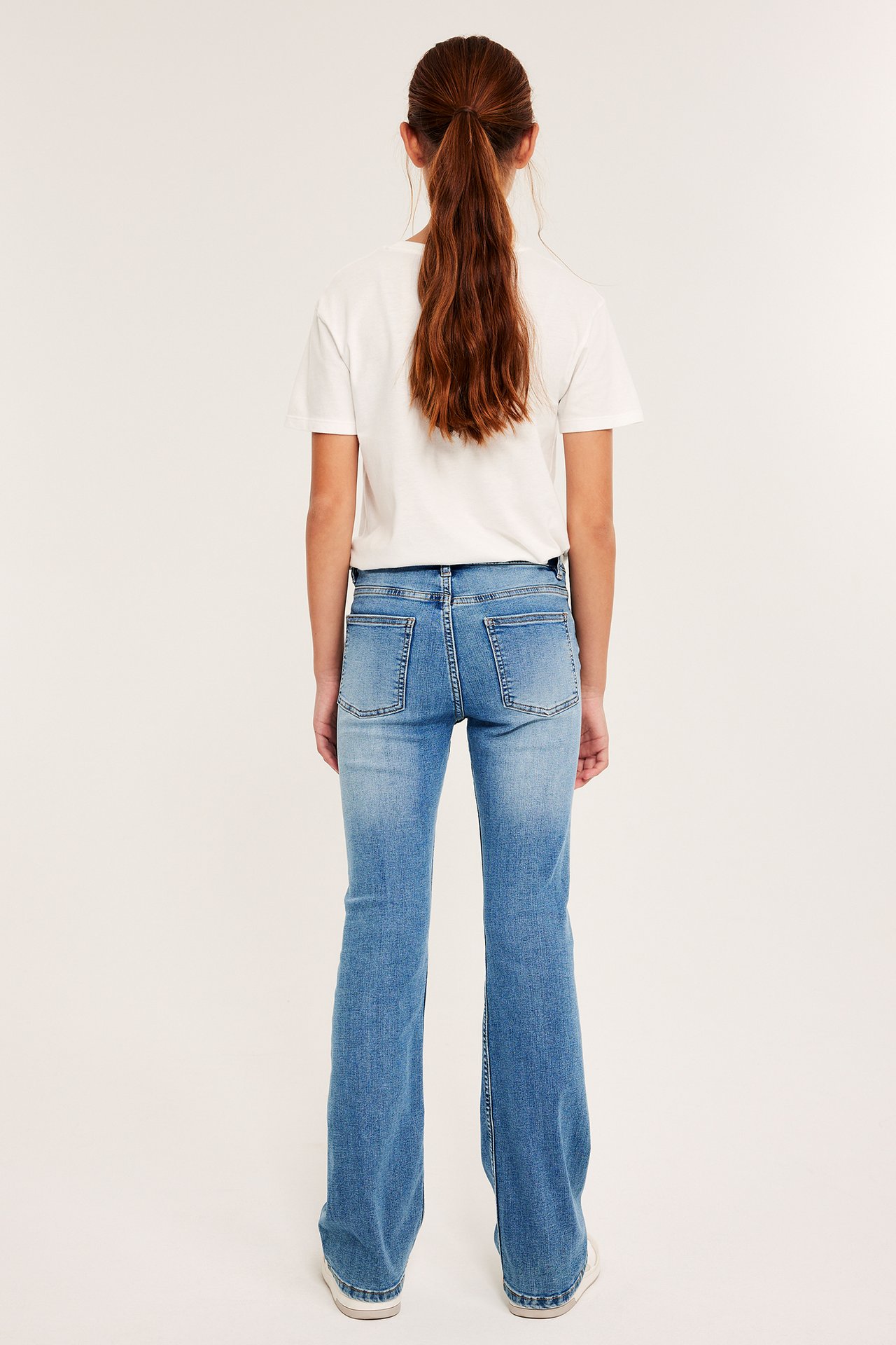 Naismallinen malli valkoisessa t-paidassa ja vaaleansinisissä bootcut-jeanseissa.