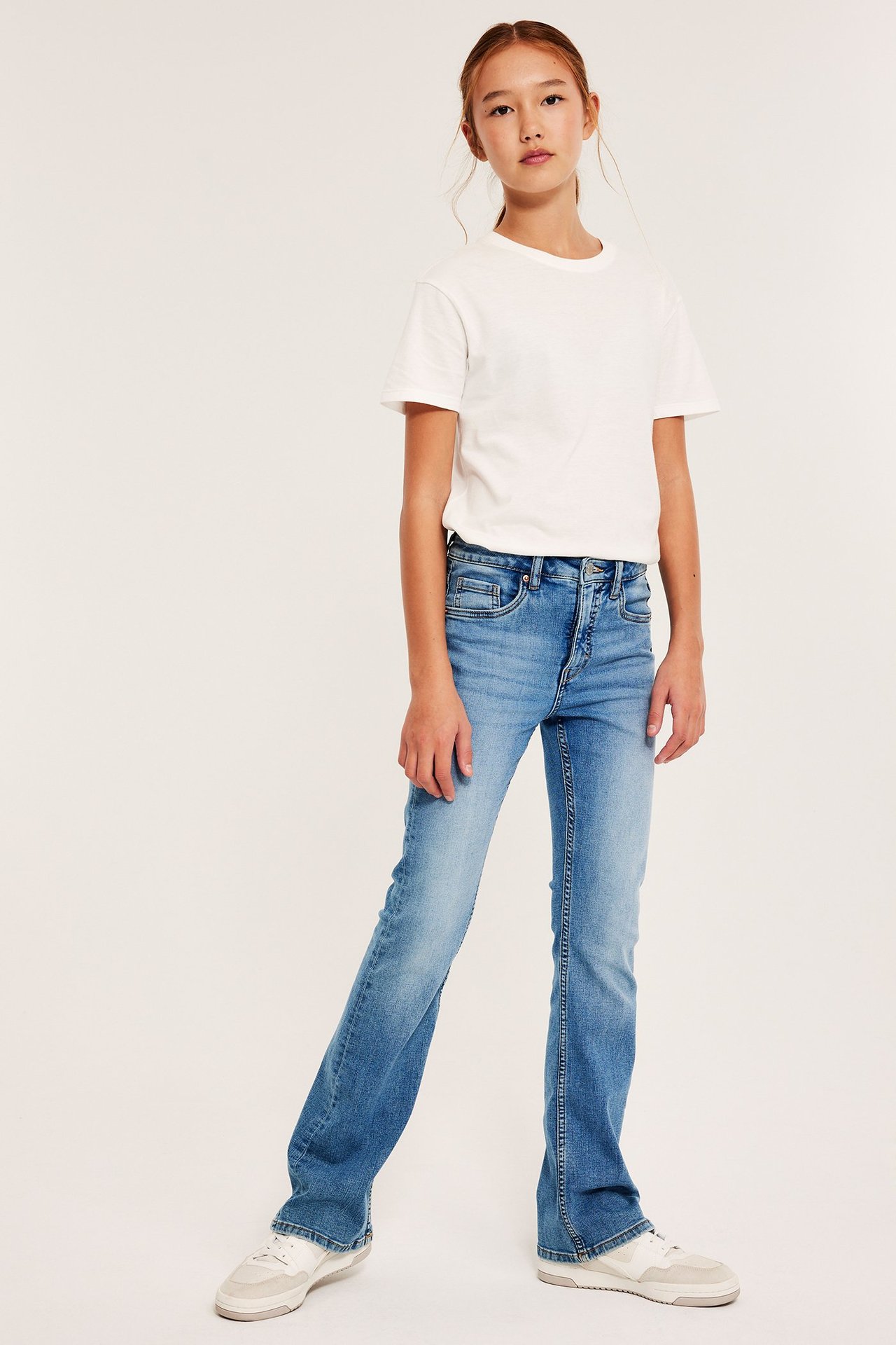 Tyttö valkoisessa T-paidassa ja vaaleansinisissä bootcut-farkuissa, keskikorkeassa vyötärössä.