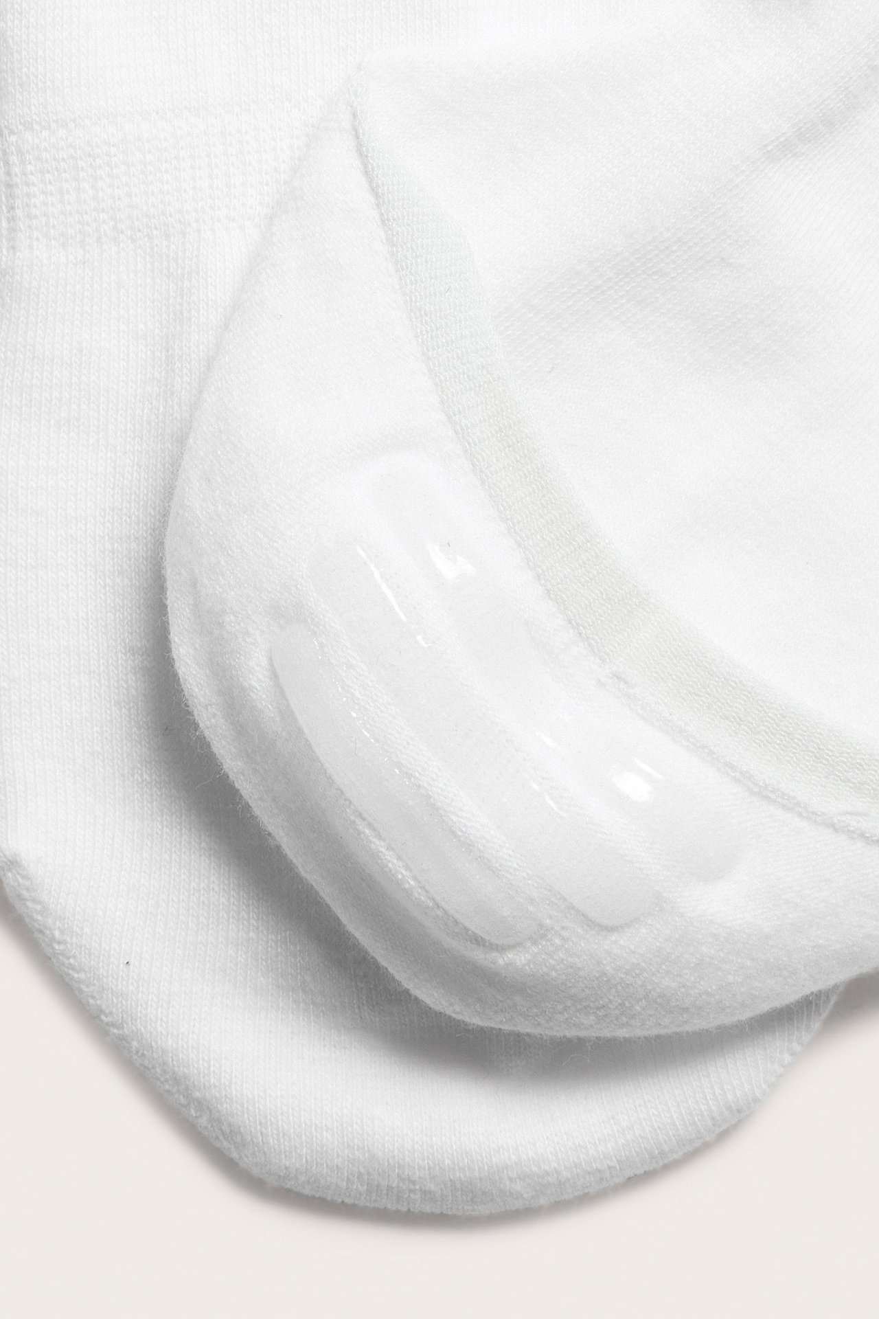 Zbliżenie białych niewidzialnych skarpetek, pokazujące silikonowy uchwyt po wewnętrznej stronie pięty.