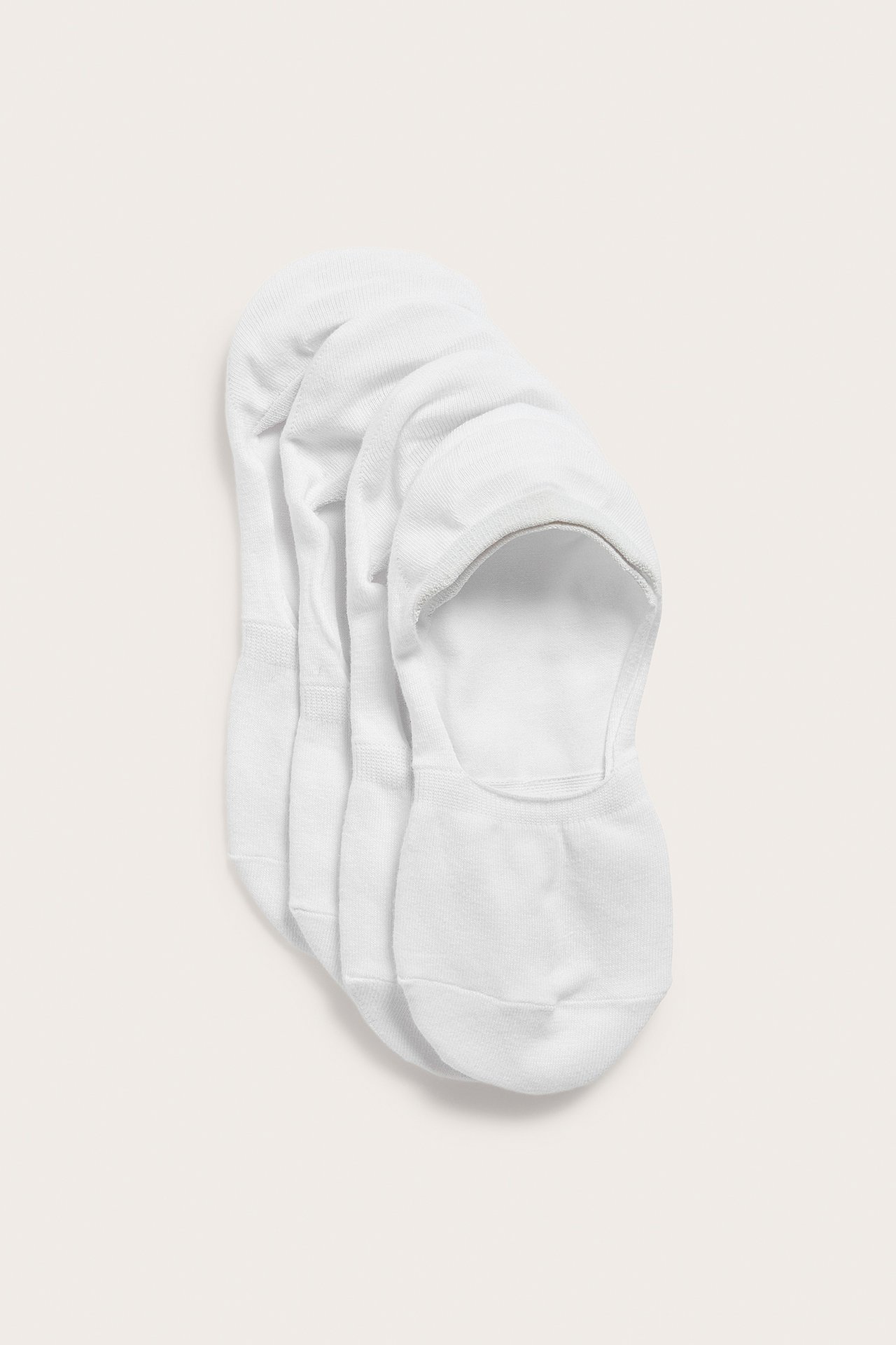 Uppifrån sett, ett 4-pack vita osynliga strumpor i bomullsblandning, staplade ovanpå varandra.
