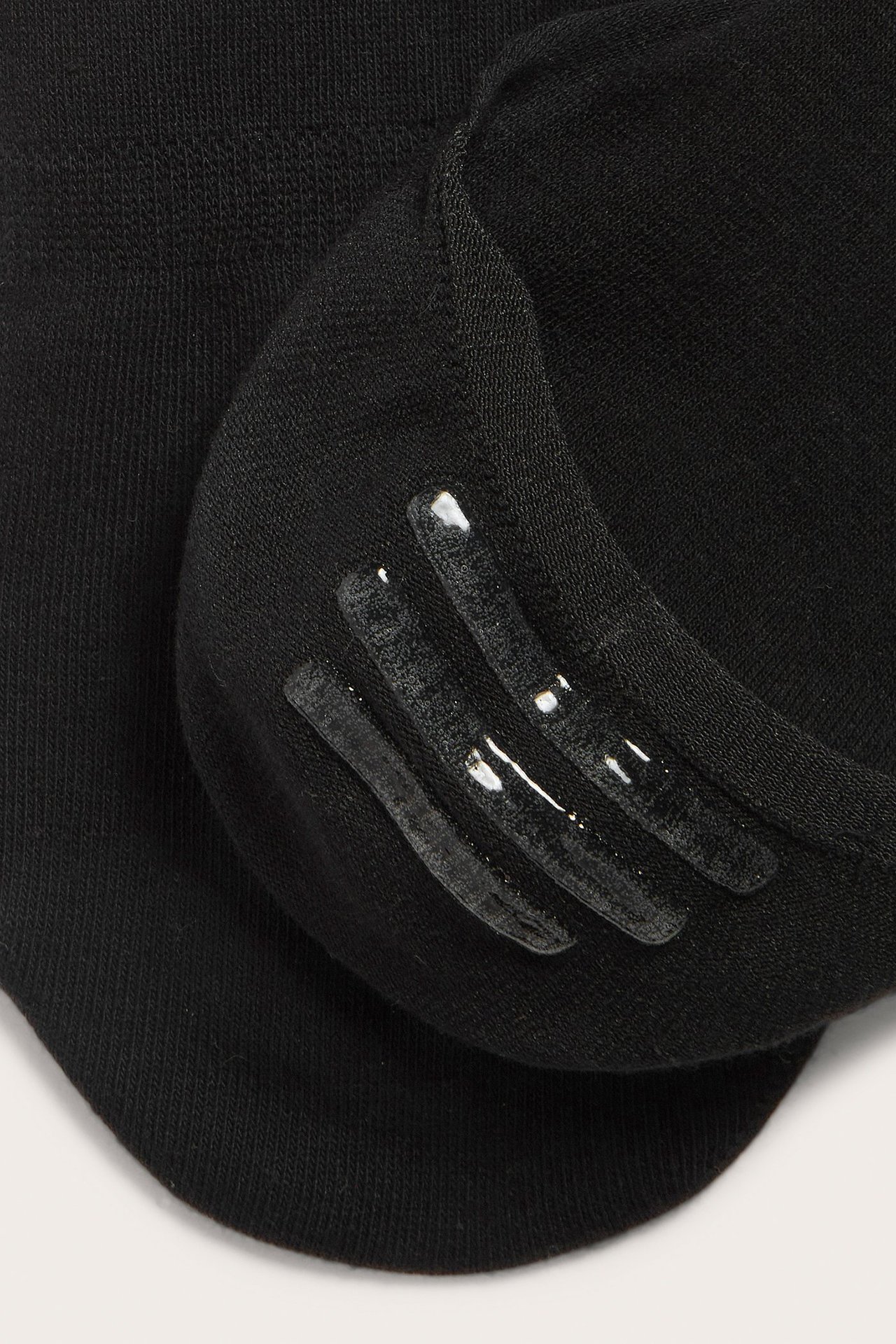 Zbliżenie: czarne niewidoczne skarpetki z silikonowymi paskami po wewnętrznej stronie pięty.