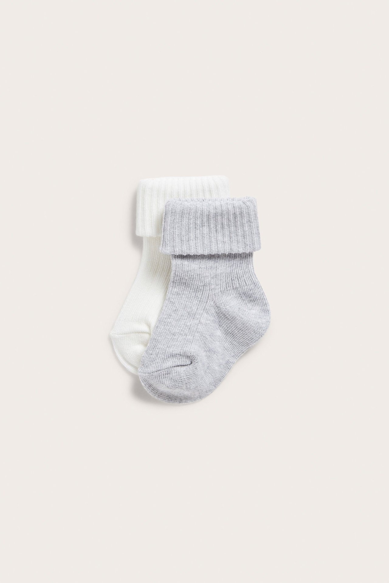 Nærbilde av to ribbestrikkede babysokker, en offwhite og en lys grå, med brettede mansjetter.