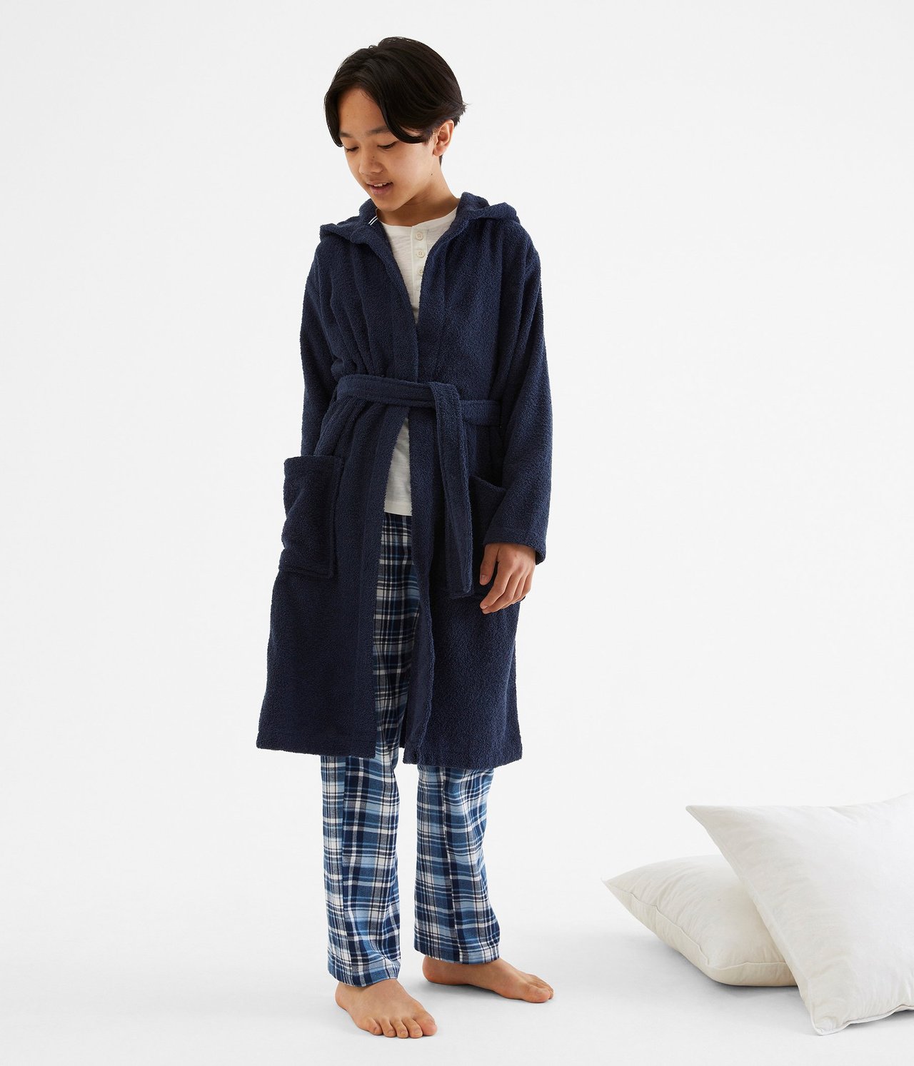 Edestäpäin, lapsi tummansinisessä hupullisessa froteeaamutakissa valkoisen topin ja siniruudullisten pyjamahousujen päällä.