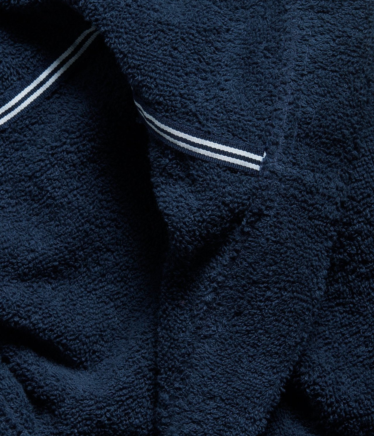 Zbliżenie na ciemnoniebieski szlafrok frotte z białymi podwójnymi paskami na klapie.