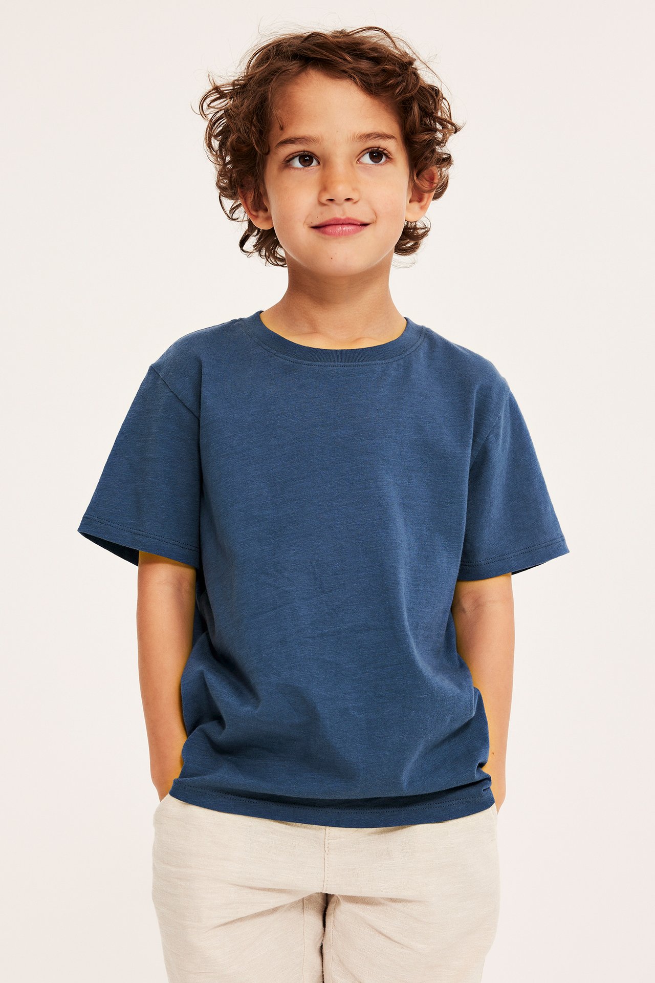 Framifrån: ett barn i mörkblå kortärmad bomulls-t-shirt och ljusbeige shorts.