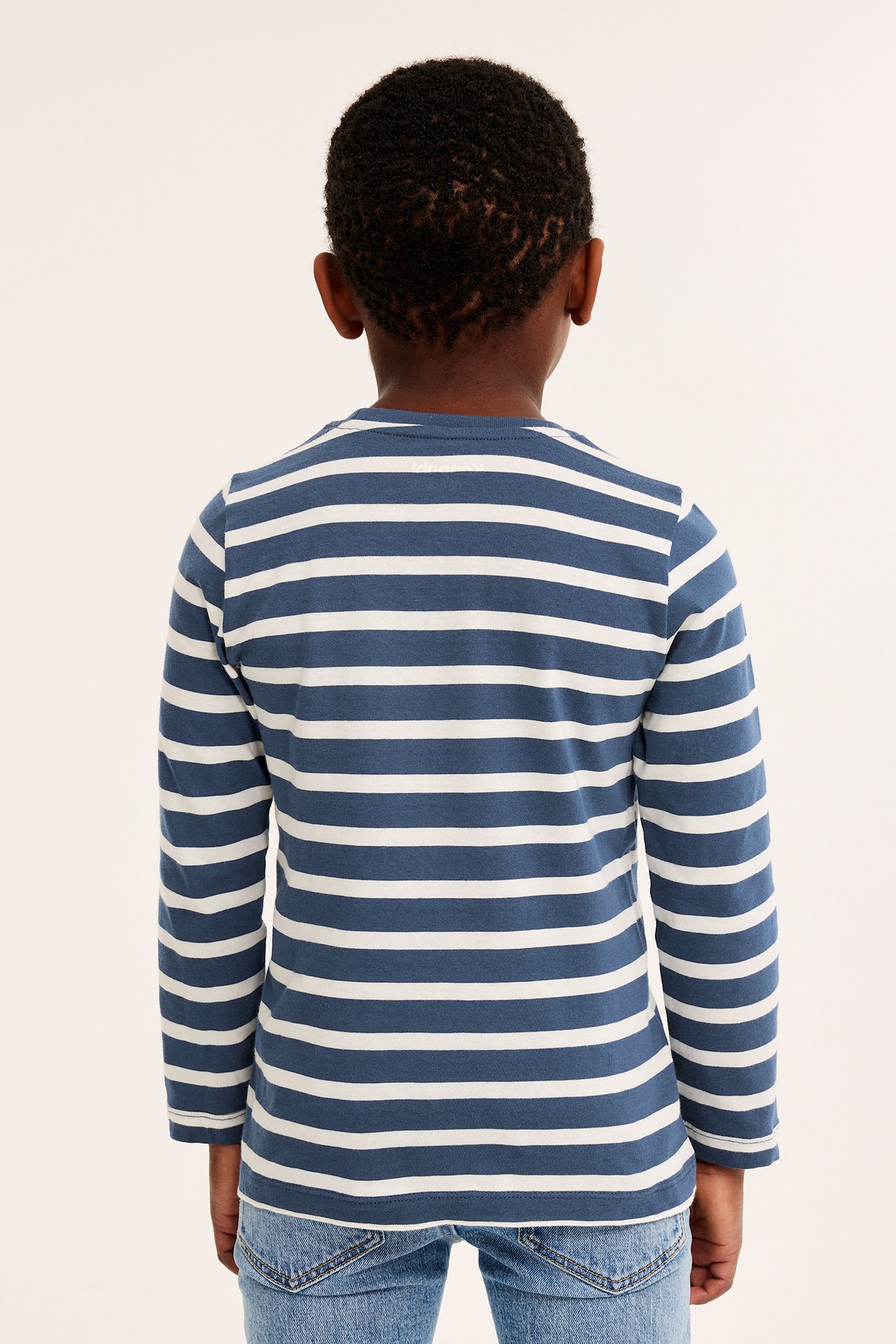 Bakifrån: ett barn i en mörkblå och vitrandig långärmad bomulls-t-shirt och blå jeans.