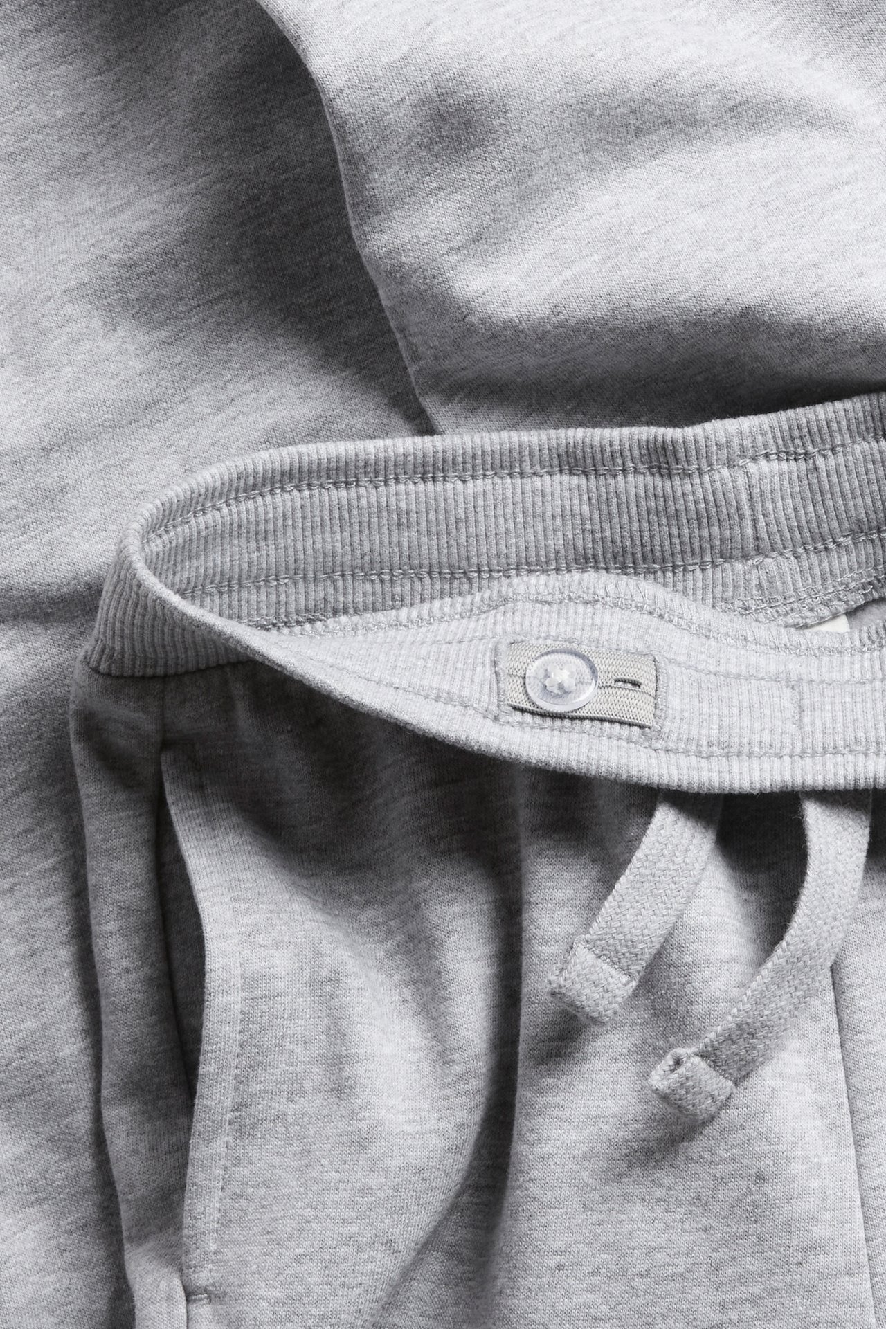 Zbliżenie szarych melanżowych spodni dresowych dla dzieci z prążkowanym pasem, sznurkiem i kieszenią.