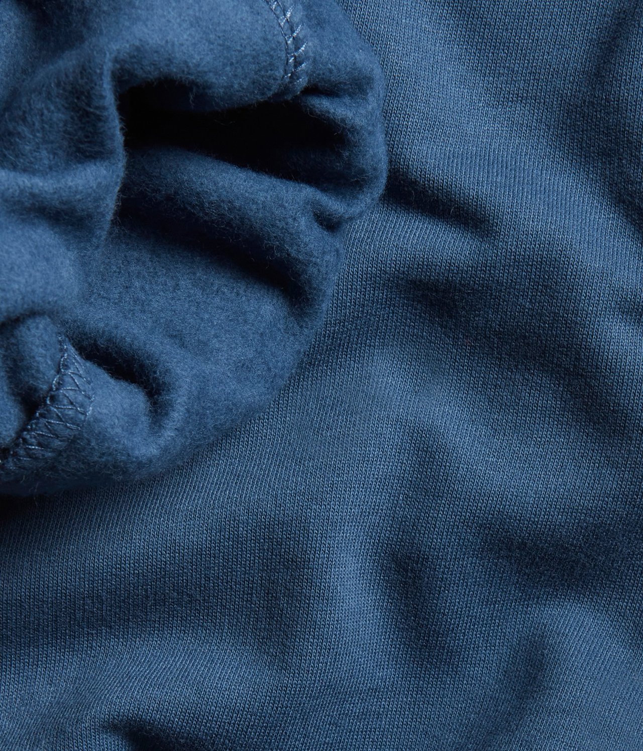 Zbliżenie na ciemnoniebieskie bawełniane spodnie dresowe, ukazujące prążkowaną i miękką, szczotkowaną fakturę.
