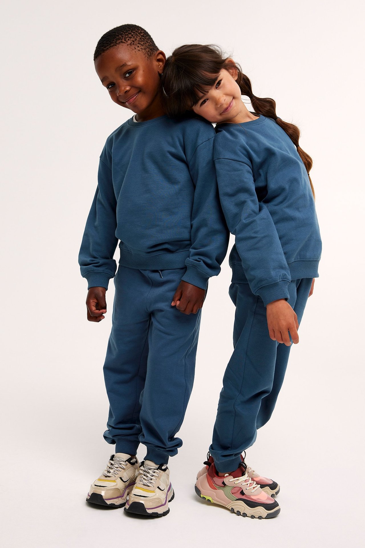 Edestä: poika ja tyttö yllään yhteensopivat tummansiniset puuvillapaidat ja collegehousut.