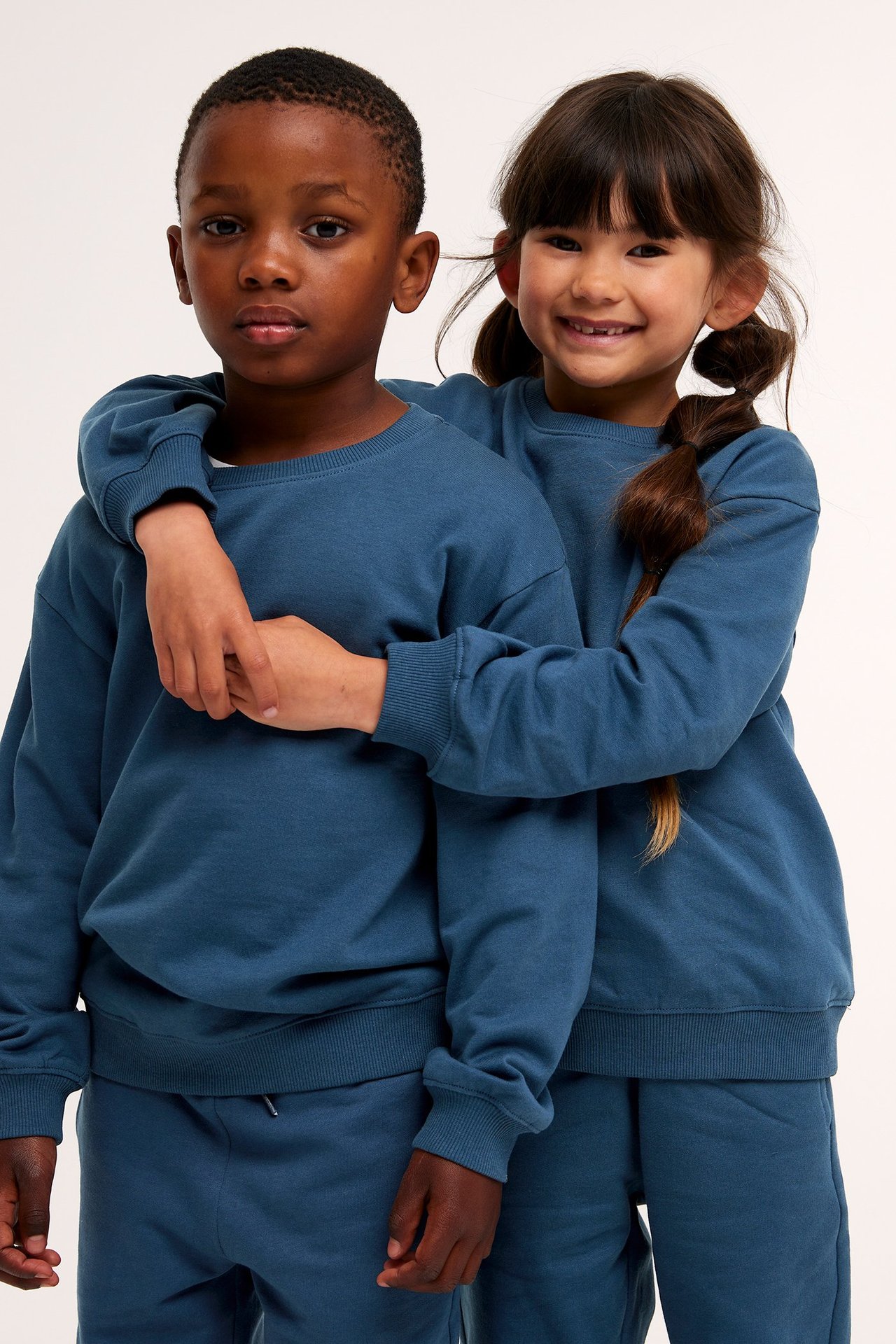 Edestäpäin poika ja tyttö yllään yhteensopivat tummansiniset puuvillafleecepaidat ja collegehousut.