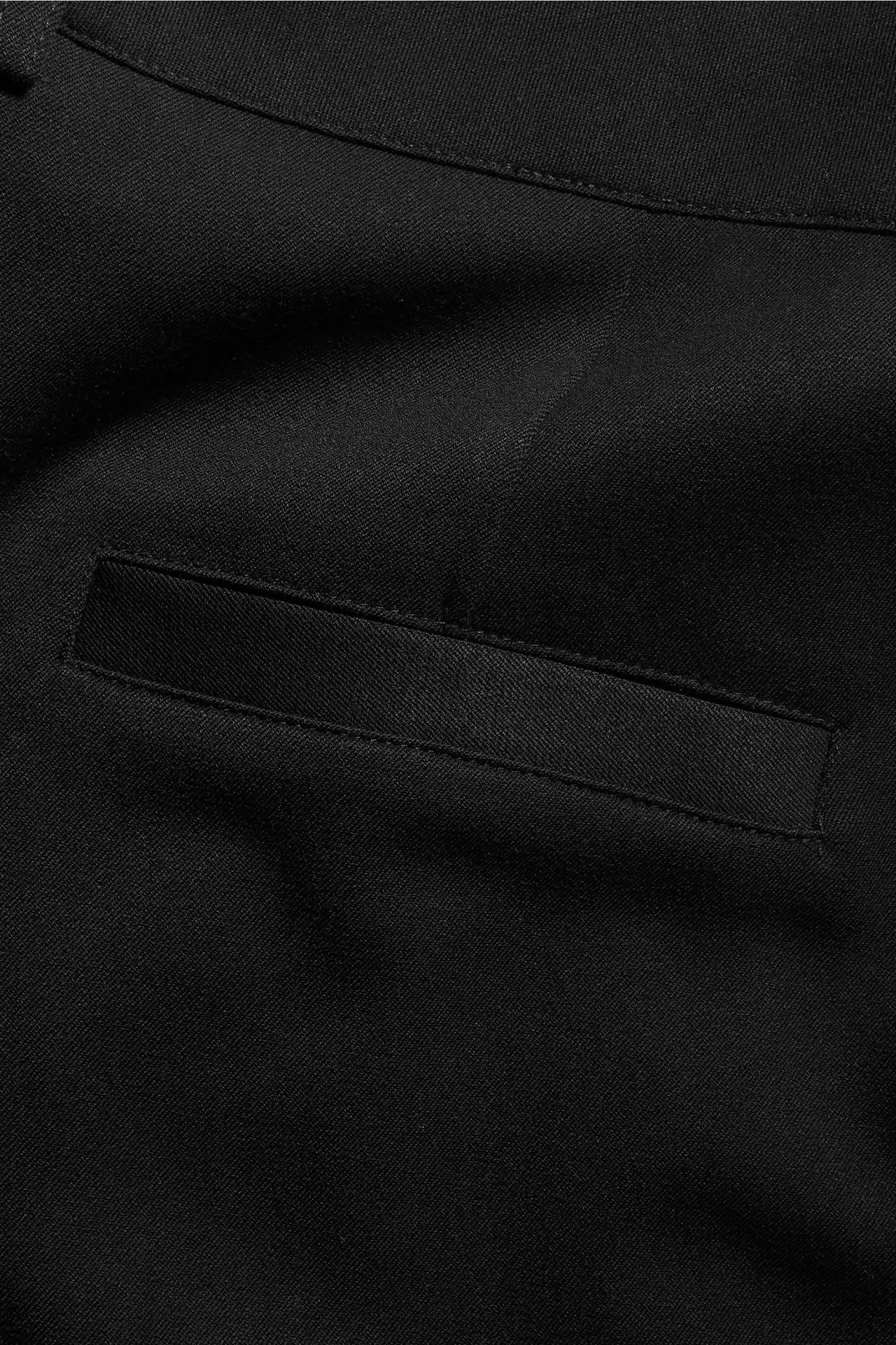 Zbliżenie na czarne, jednolite spodnie garniturowe z widoczną poziomą kieszenią paspoalową.