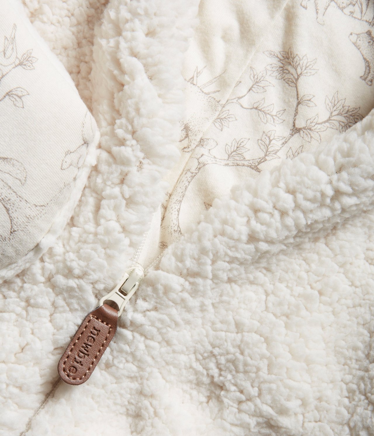 Zbliżenie białego pluszowego kombinezonu niemowlęcego z zamkiem i wzorzystą podszewką dżersejową.