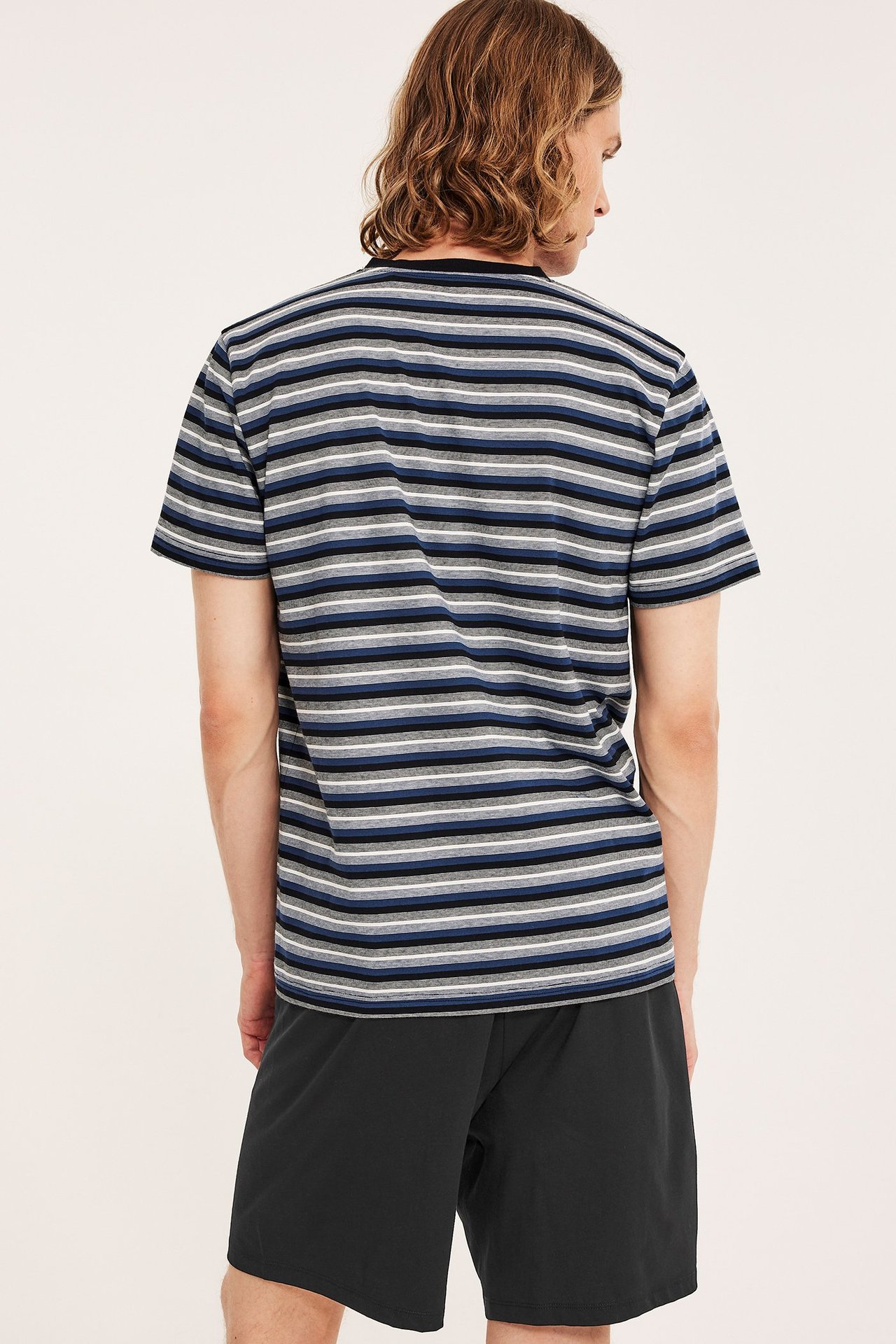 Bakifrån: man i svarta jersey-pyjamasshorts och en randig t-shirt.