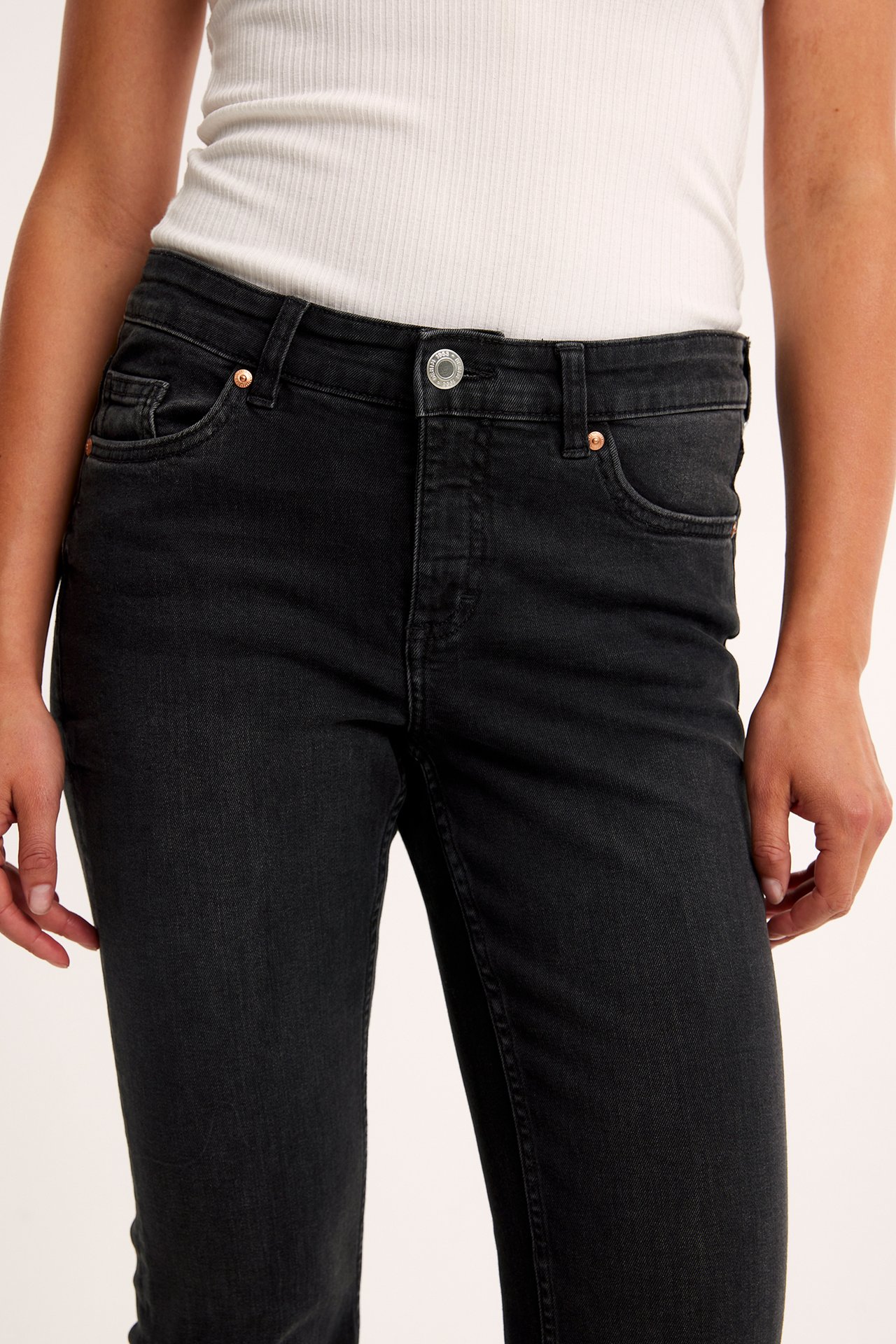Zbliżenie z przodu kobiety w czarnych jeansach bootcut z niskim stanem i białym prążkowanym topie.