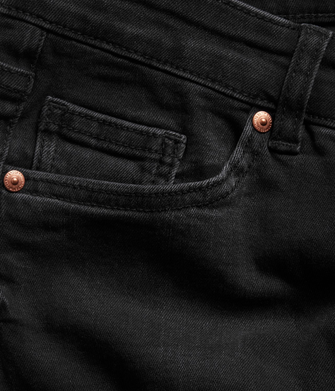 Zbliżenie na czarne dżinsy bootcut z denimu, pokazujące przednią kieszeń z miedzianymi nitami.
