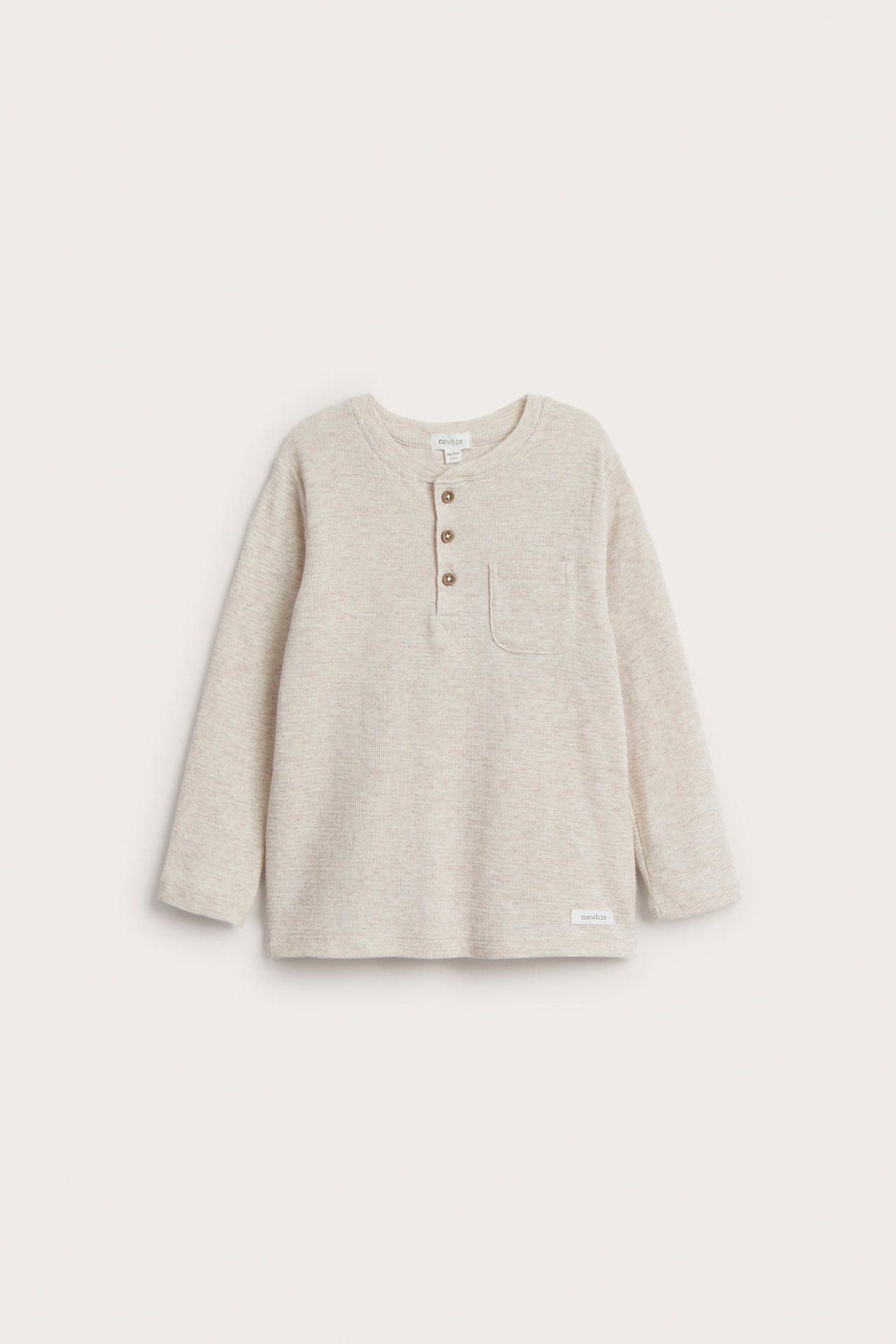 Framifrån, en barnslångärmad ljusbeige strukturerad henleyskjorta med tre knappar och bröstficka.