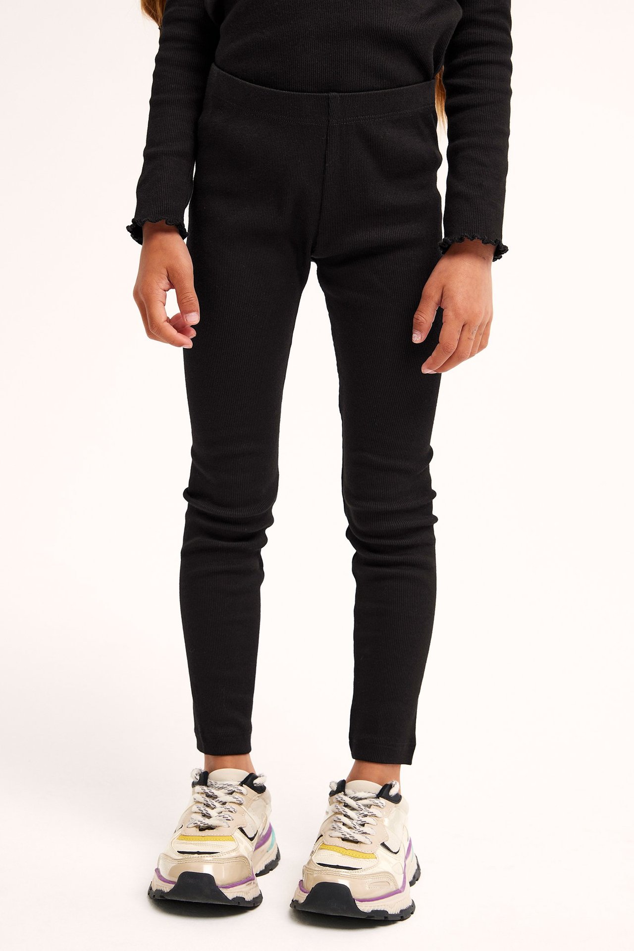 Edestä: lapsi mustissa ribbileggingseissä, pitkähihaisessa paidassa ja beigenvärisissä lenkkareissa.