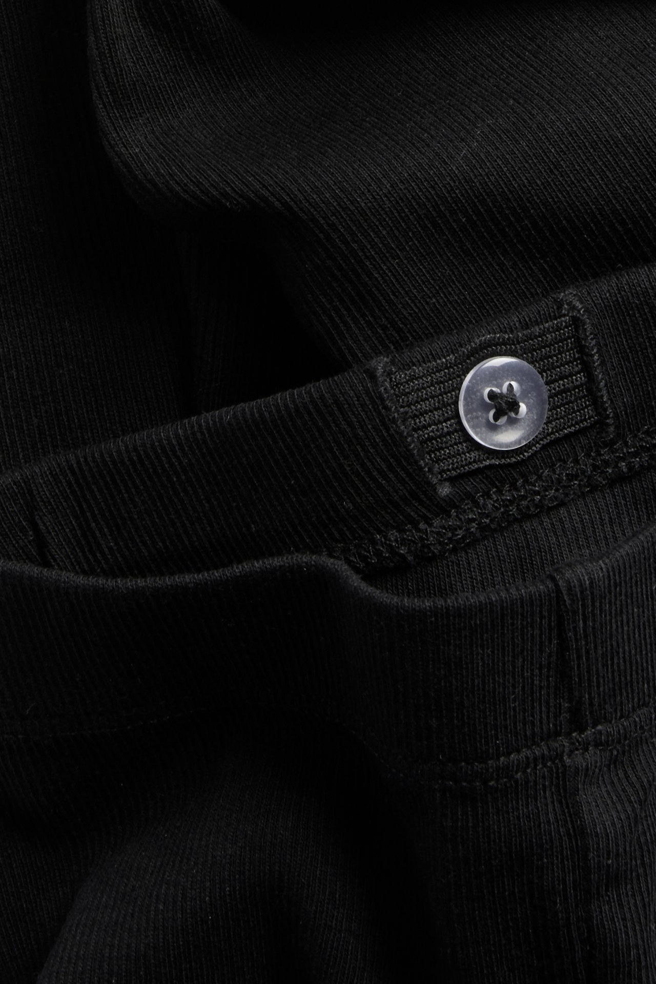 Mustien ribattujen leggingsien lähikuva, säädettävä vyötärö ja läpinäkyvä nappi.