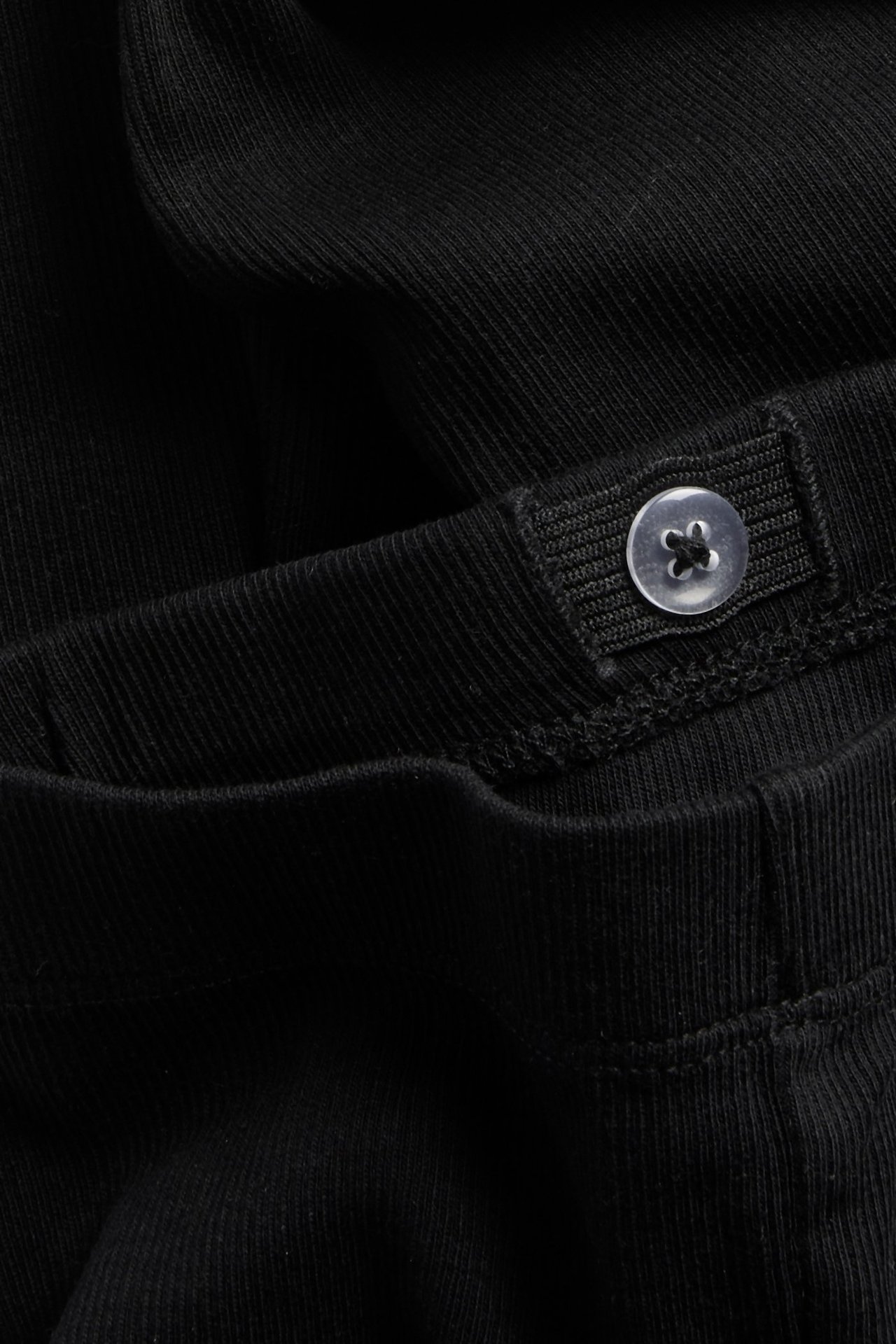 Zbliżenie na czarne prążkowane legginsy z regulowaną talią i przezroczystym guzikiem.