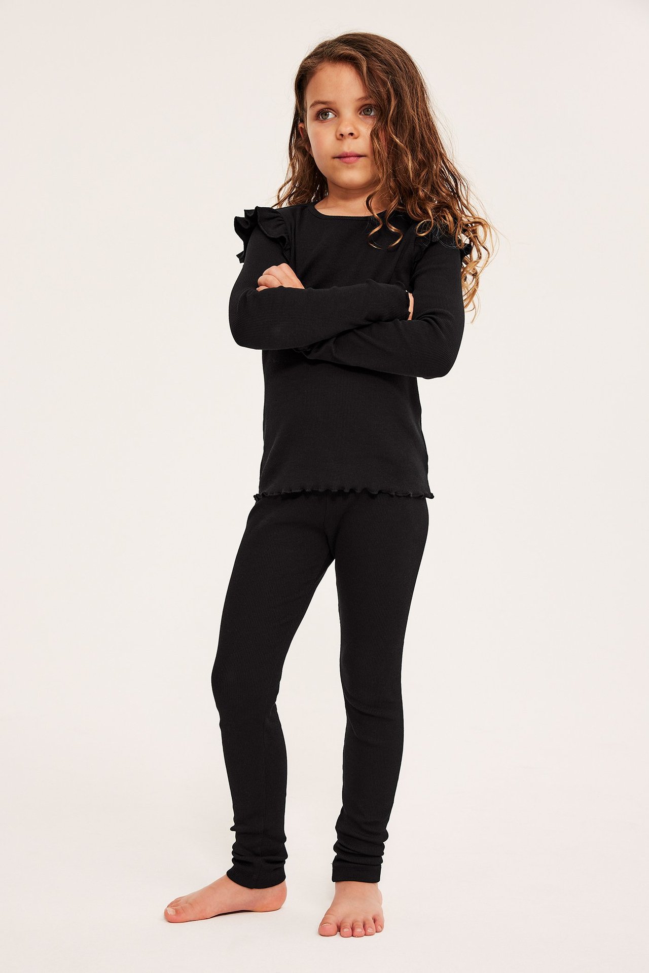 Koko etunäkymä lapsesta, jolla on mustat ribbileggingsit ja musta pitkähihainen toppi röyhelöillä.