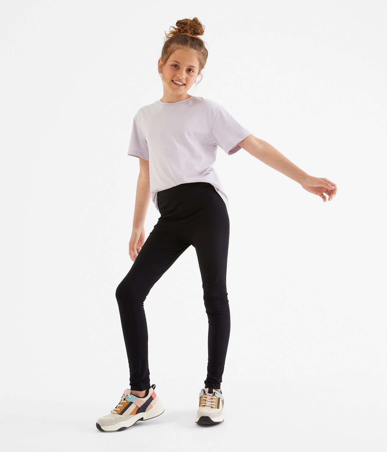 Edestäpäin: lapsi mustissa slim-fit leggingseissä, vaaleanliilassa t-paidassa ja monivärisissä lenkkareissa.