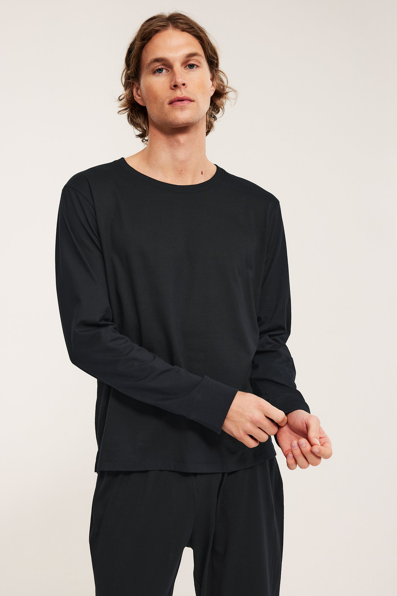 Forfra: mann i svart ensfarget pyjamasoverdel i bomull og matchende svart pyjamasbukse.