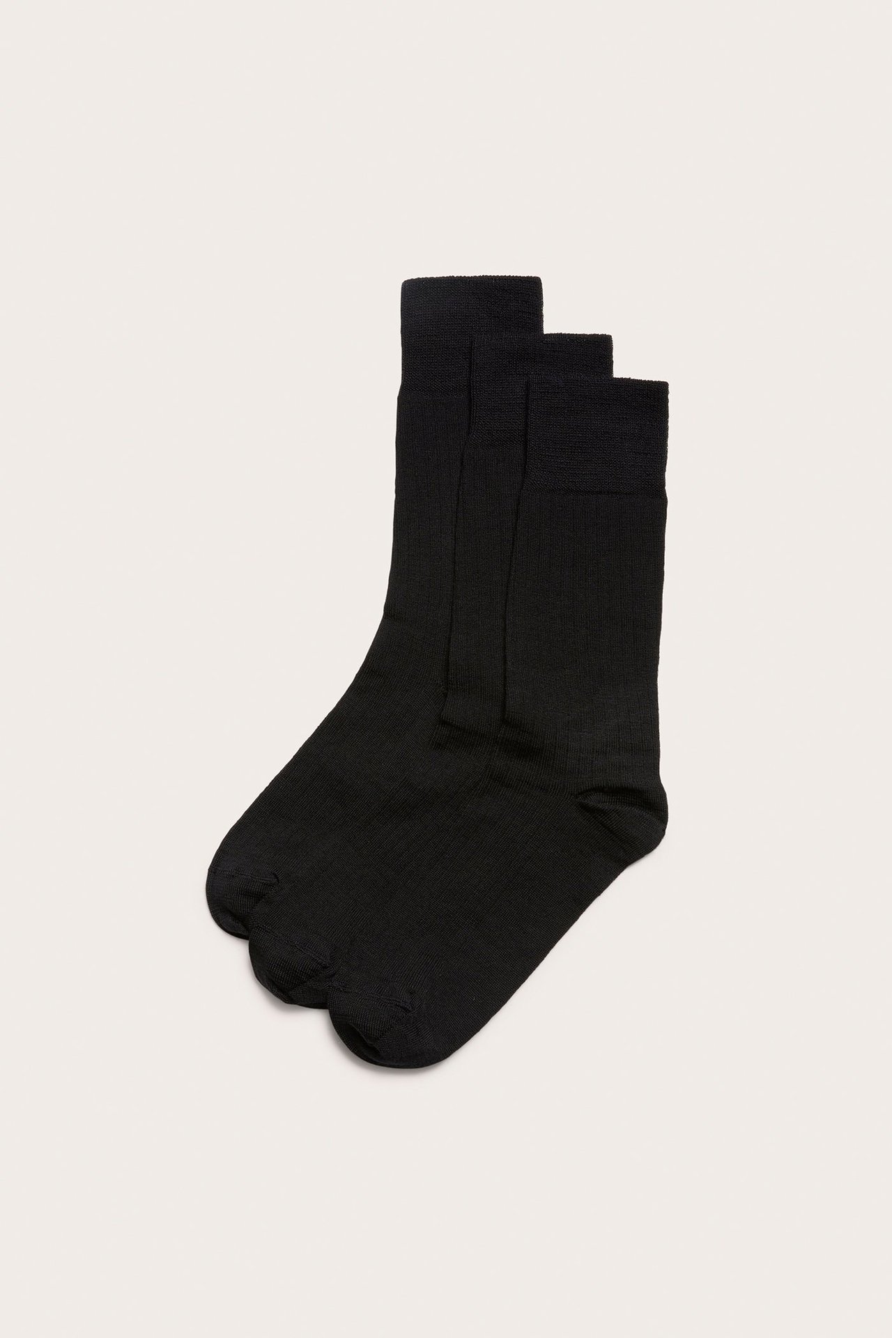 Edestä näkymä kolmesta mustasta sileäneuleisesta sukasta, joissa resorit, pinottuna.