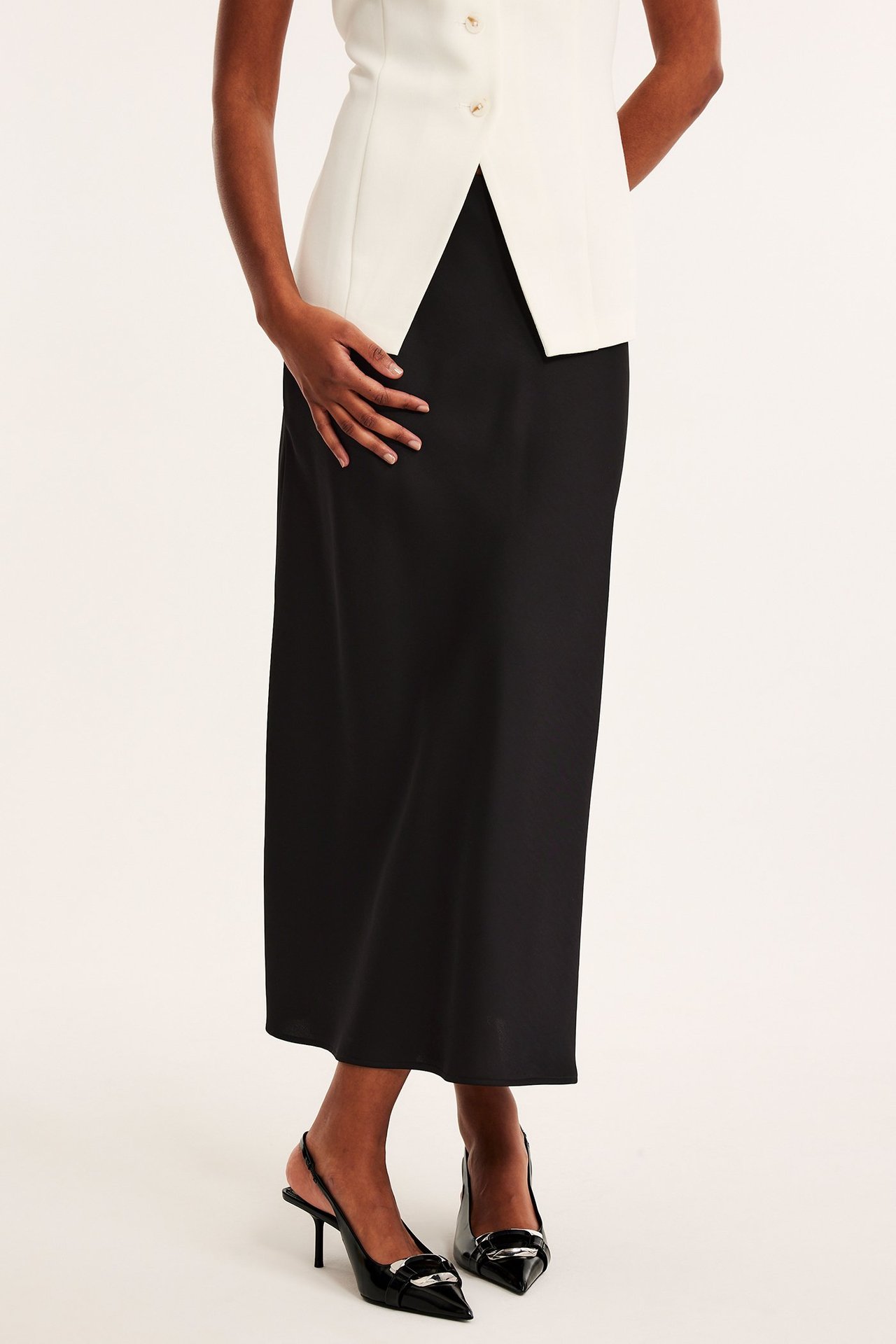 Forfra: kvinne i svart utsvingt satengskjørt, hvit ermeløs topp og svarte slingback-hæler.