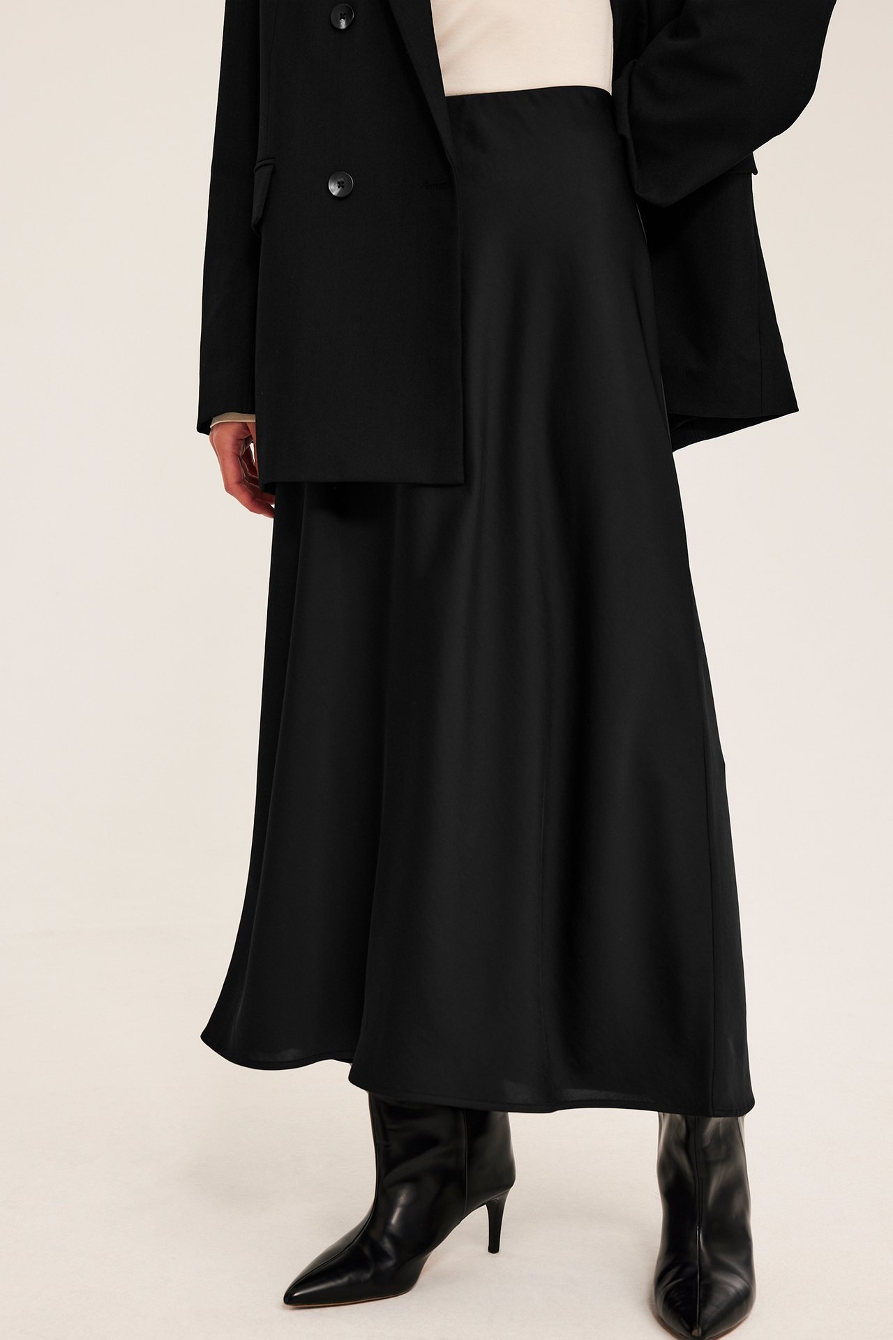 Frontvy av en kvinna i svart midikjol, svart kavaj och svarta ankelboots.