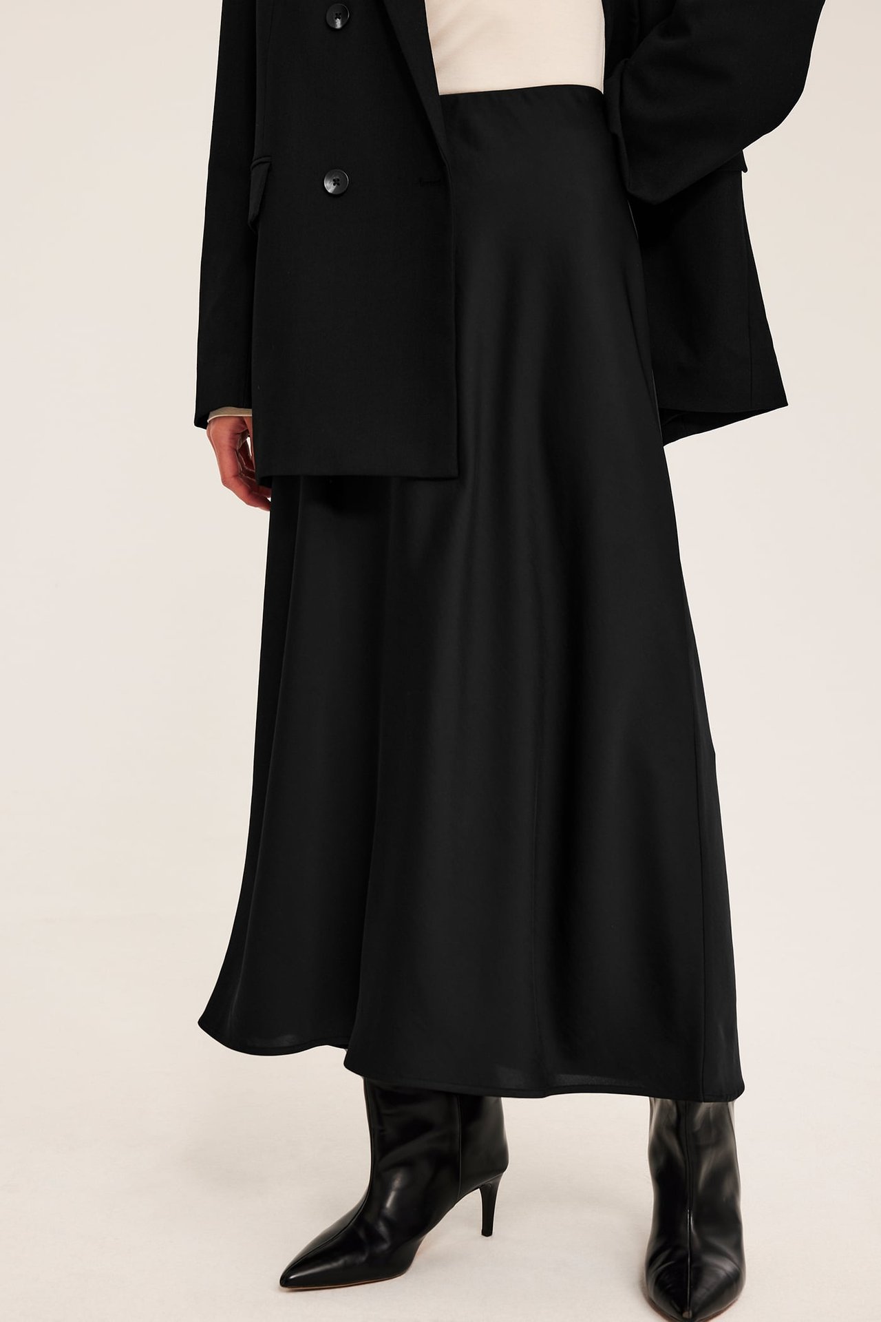 Frontvy av en kvinna i svart midikjol, svart kavaj och svarta ankelboots.