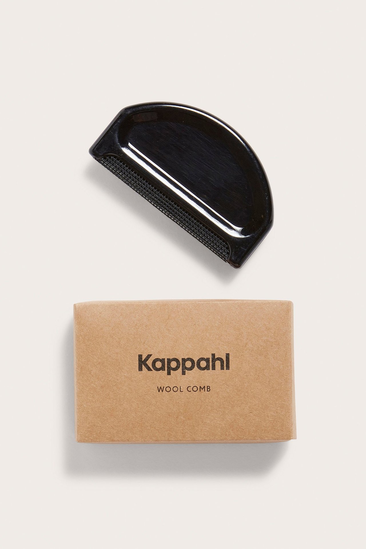Svart ullkam med plastkropp, över ett beige förvaringsfodral.