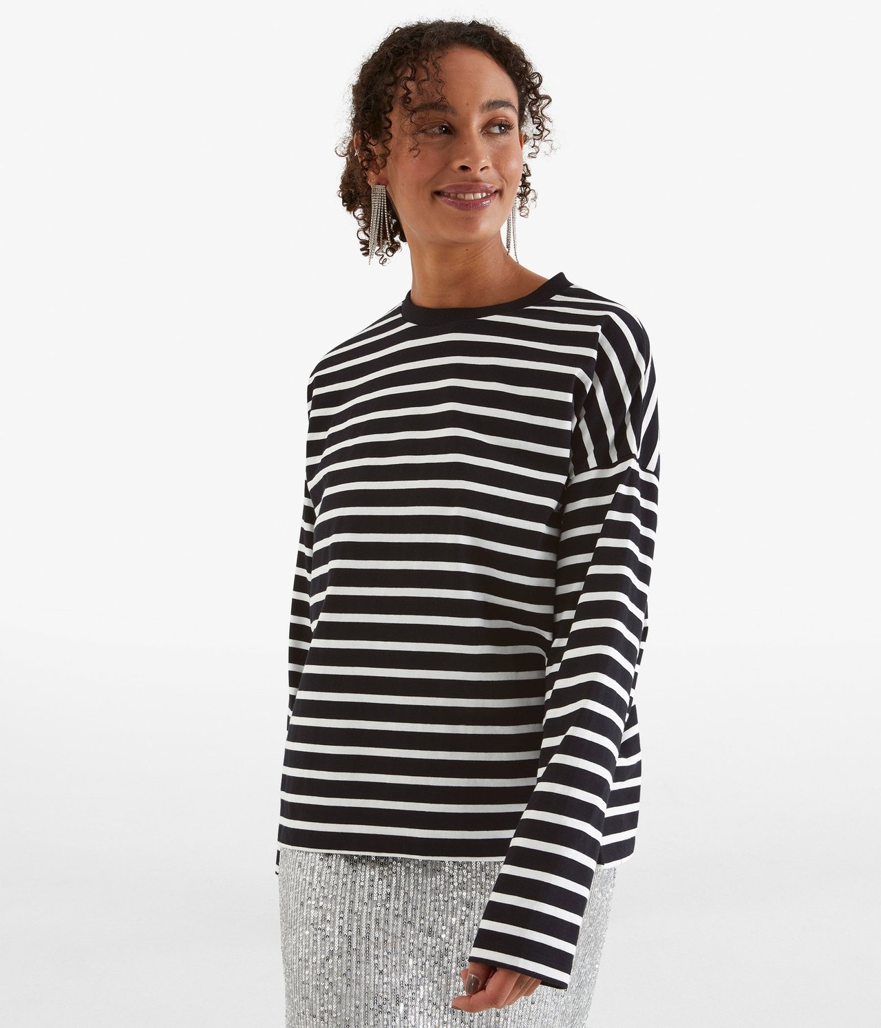 Forfra: kvinne i svart- og hvitstripet langermet topp, sølvpaljettskjørt og dinglende sølvøreringer.