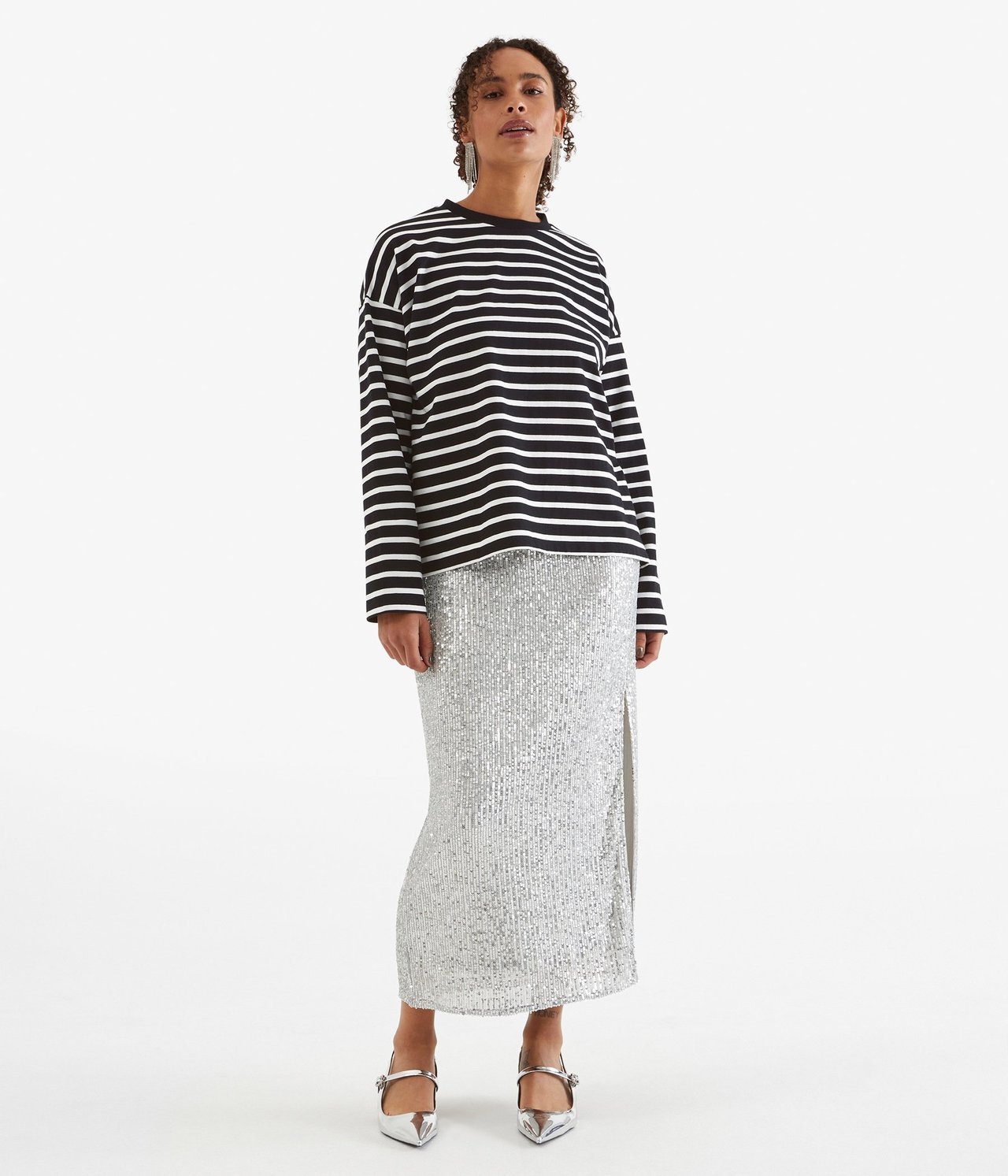 Widok z przodu: Kobieta w luźnym czarno-białym topie bawełnianym w paski, srebrnej spódnicy cekinowej i srebrnych butach.