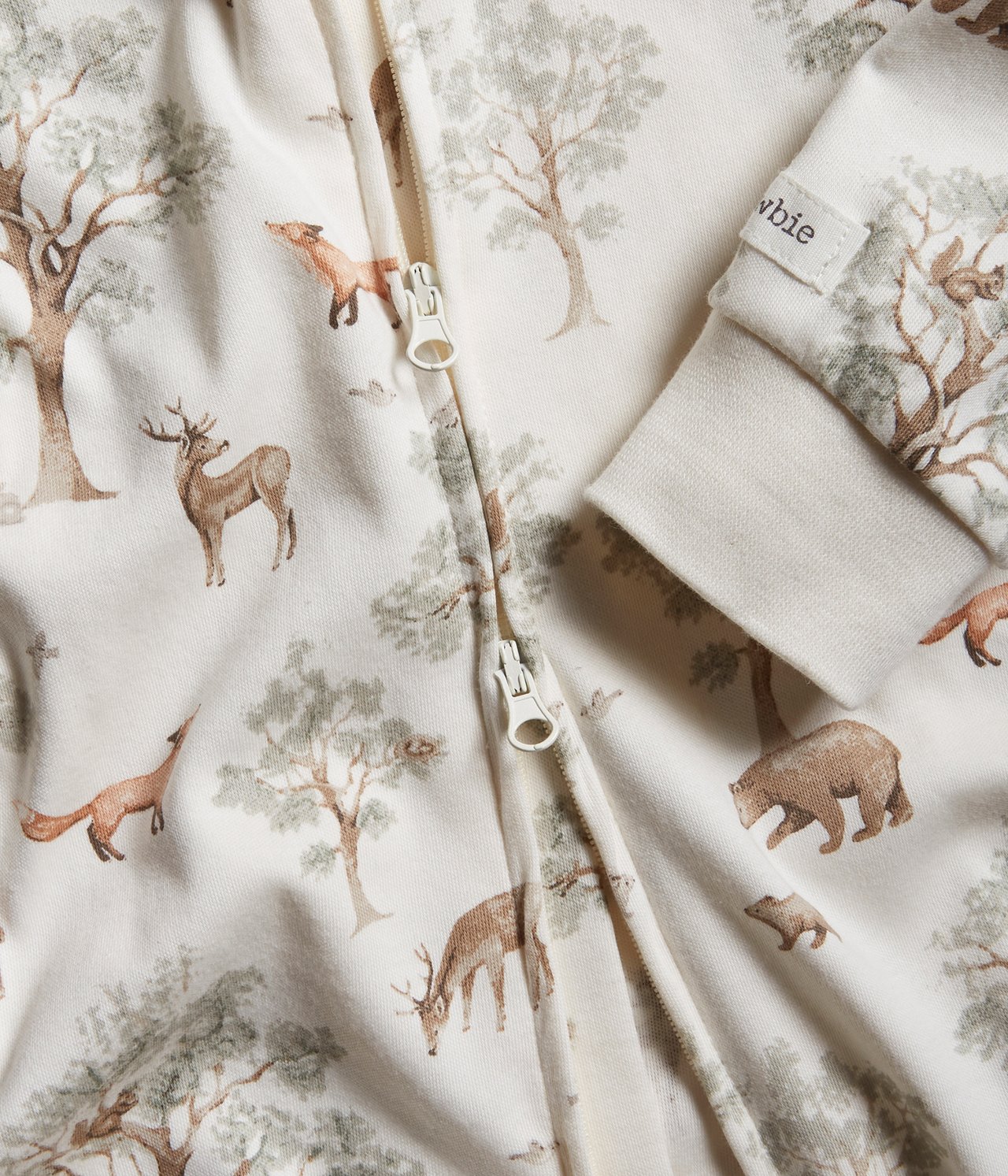 Lähikuva luonnonvalkoisesta vauvan puuvillapyjamasta, jossa on metsäkuvio ja kaksisuuntainen vetoketju.