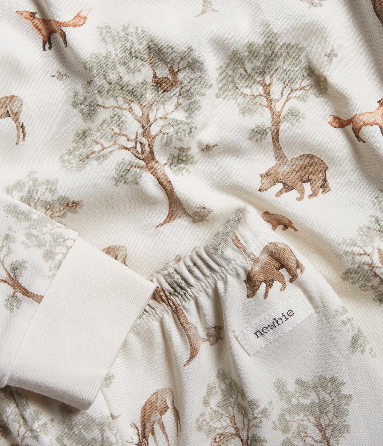 Lähikuva luonnonvalkoisesta lasten pyjamasta, jossa on ruskea-vihreä metsäeläinkuvio.