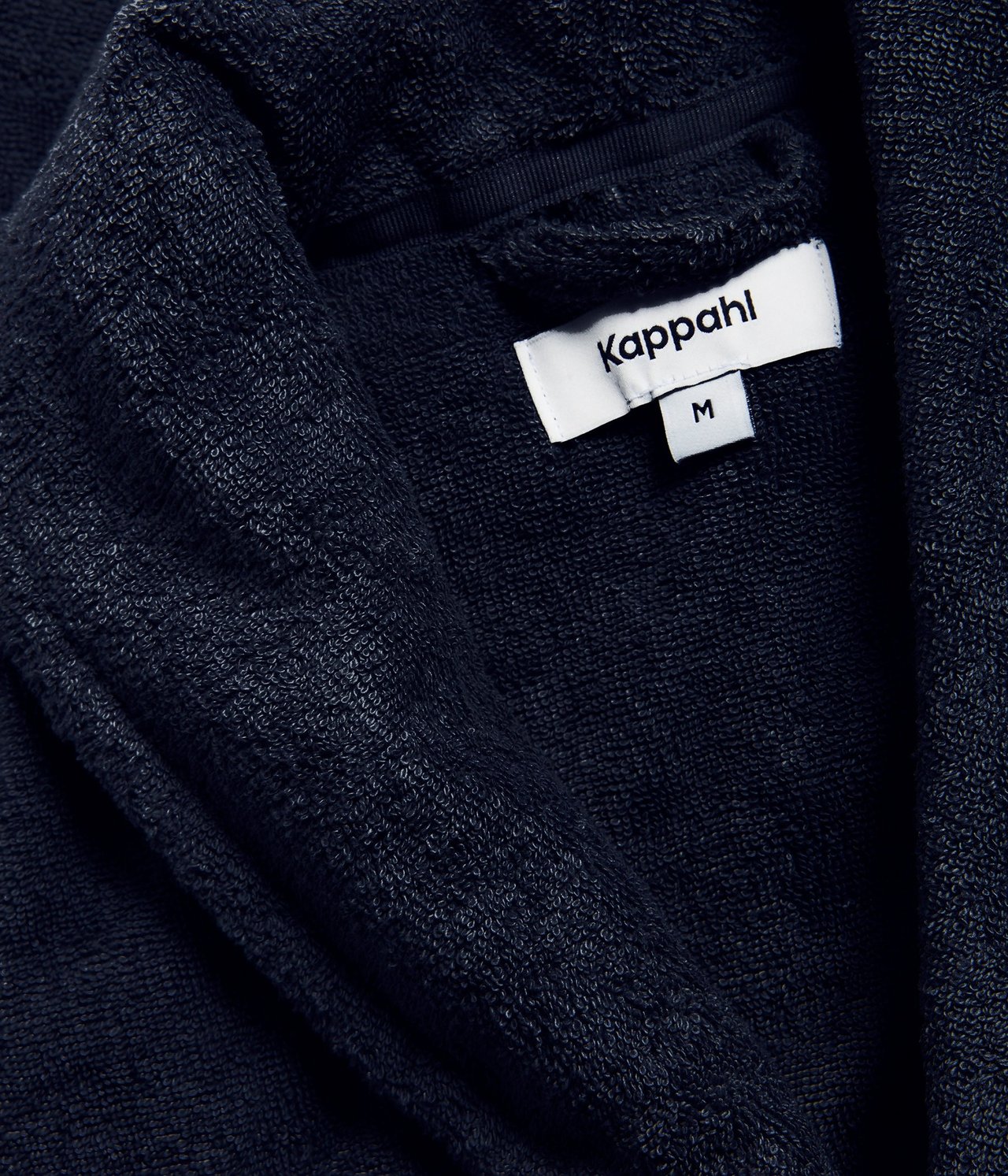 Zbliżenie na ciemnoniebieski bawełniany szlafrok frotte, ukazujące teksturę materiału i metkę z rozmiarem M.