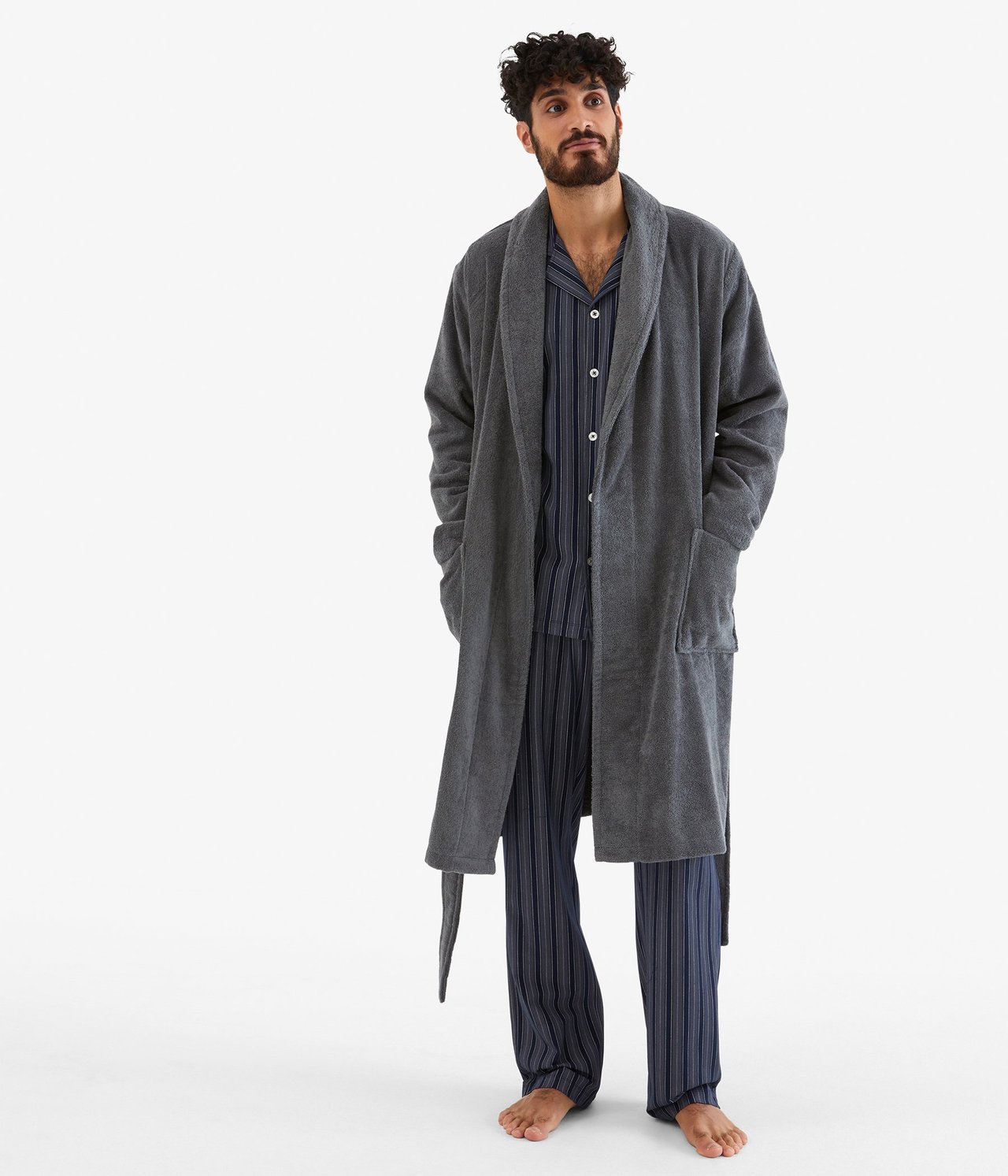 Edestä näkymä miehestä harmaassa froteekylpytakissa siniraitaisen pyjamasetin päällä.