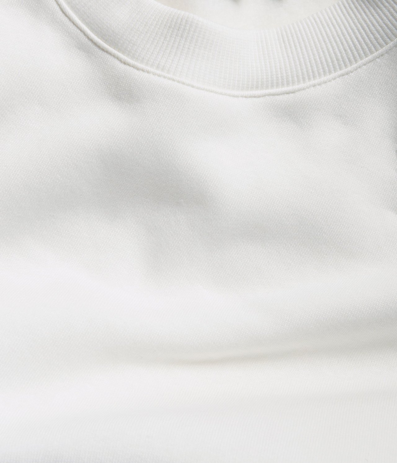 Zbliżenie na bluzę w kolorze złamanej bieli, ukazujące prążkowany okrągły dekolt i miękki materiał.