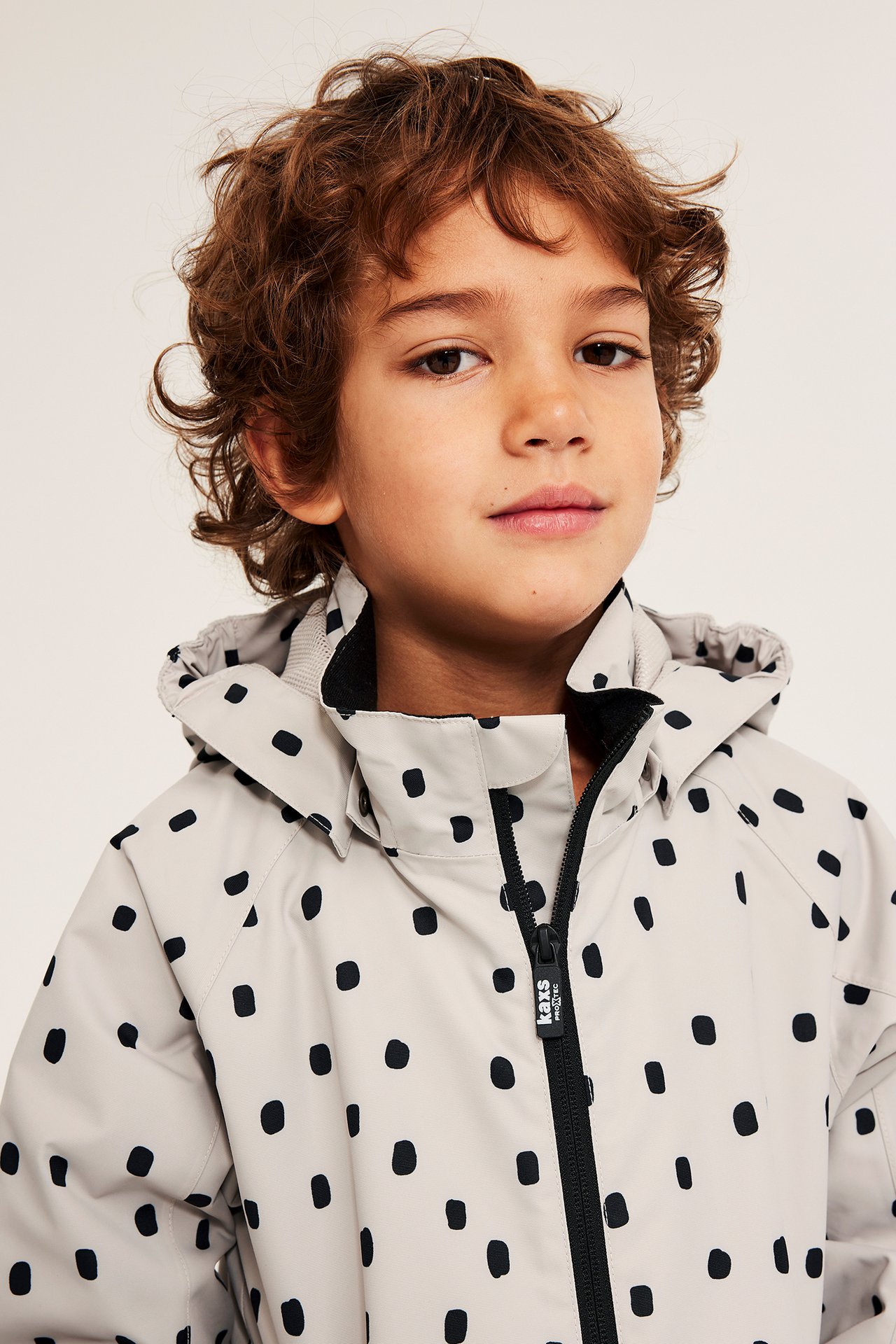 Jente i beige vannavisende jakke med svarte prikker, glidelås foran.