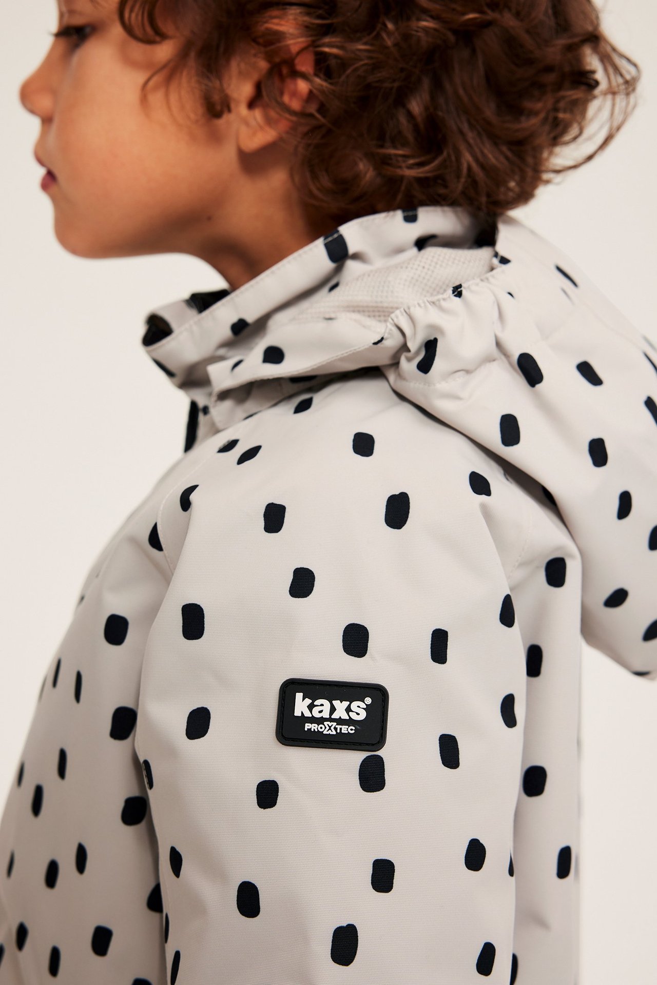 Gutt i beige, mønstret vanntett jakke med justerbare ermer og avtakbar hette.