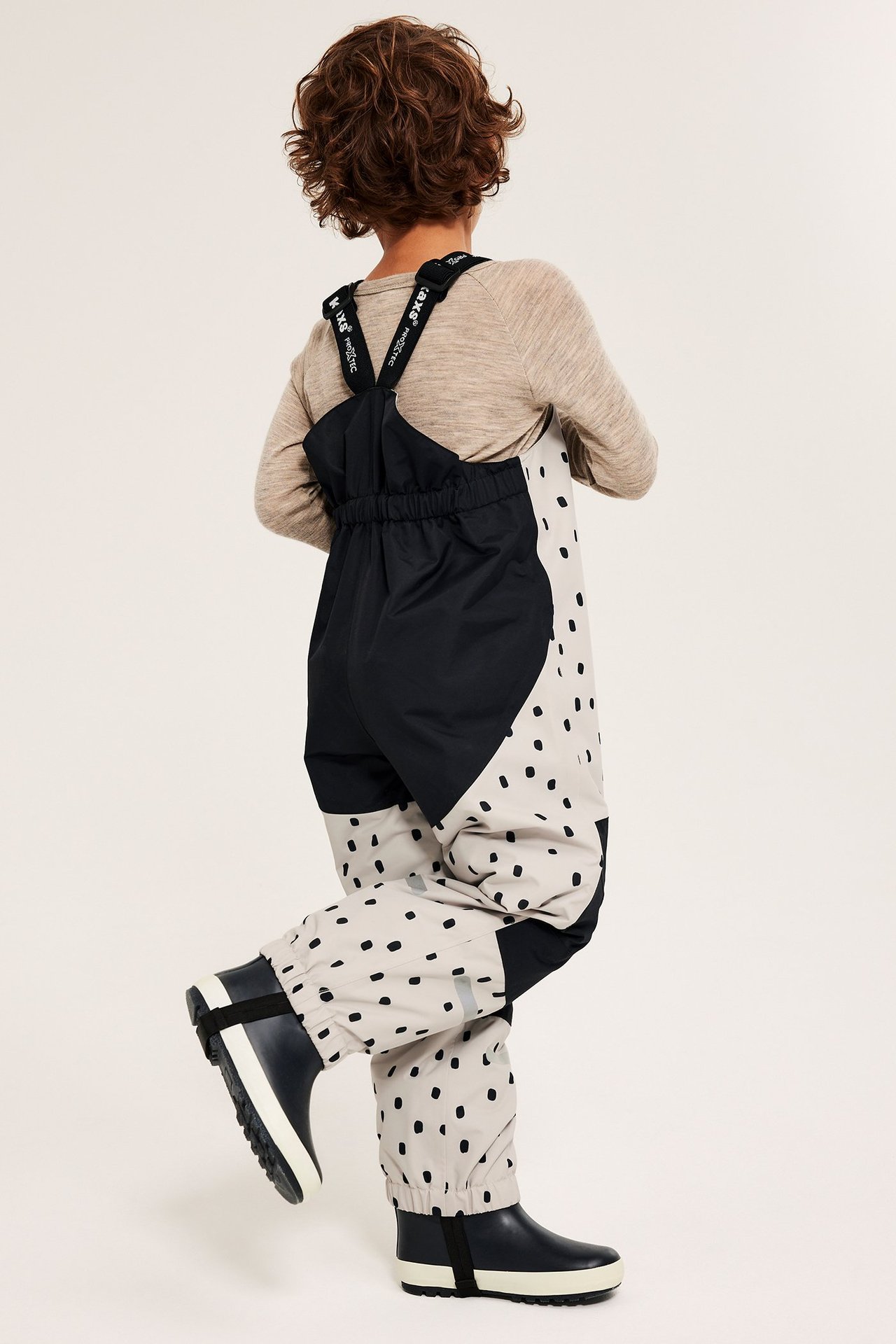 Lapsi beigeissä ja mustissa vedenpitävissä haalareissa säädettävällä koolla, kuviolliset, resorilla ja vetoketjulla.
