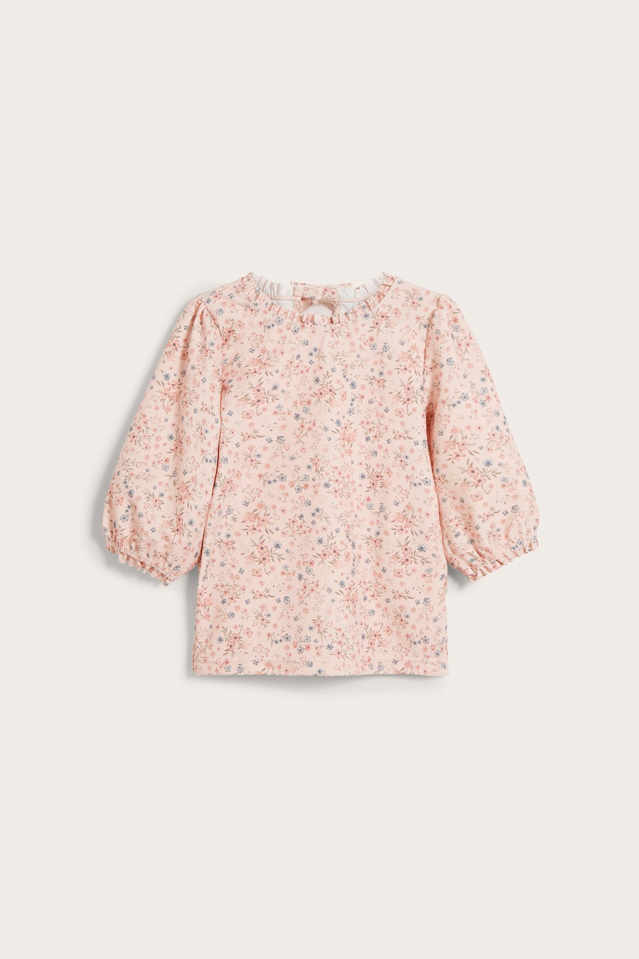 Frontvisning av en baby lyserosa blomstret UV-topp med 3/4-ermer, rysjehals og sløyfe bak.