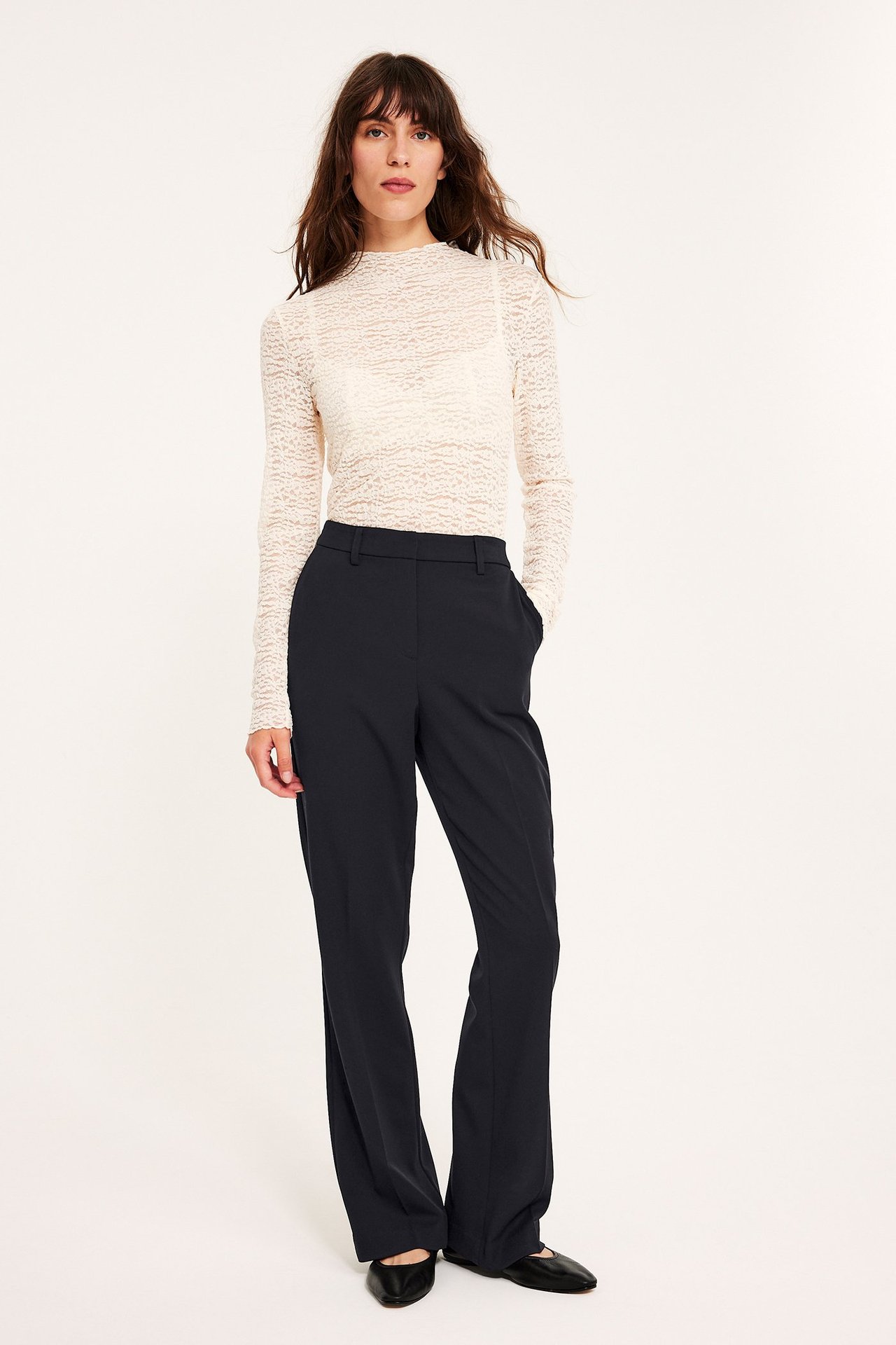 Widok z przodu: kobieta w czarnych spodniach garniturowych slim flare, białym teksturowanym topie i czarnych balerinach.