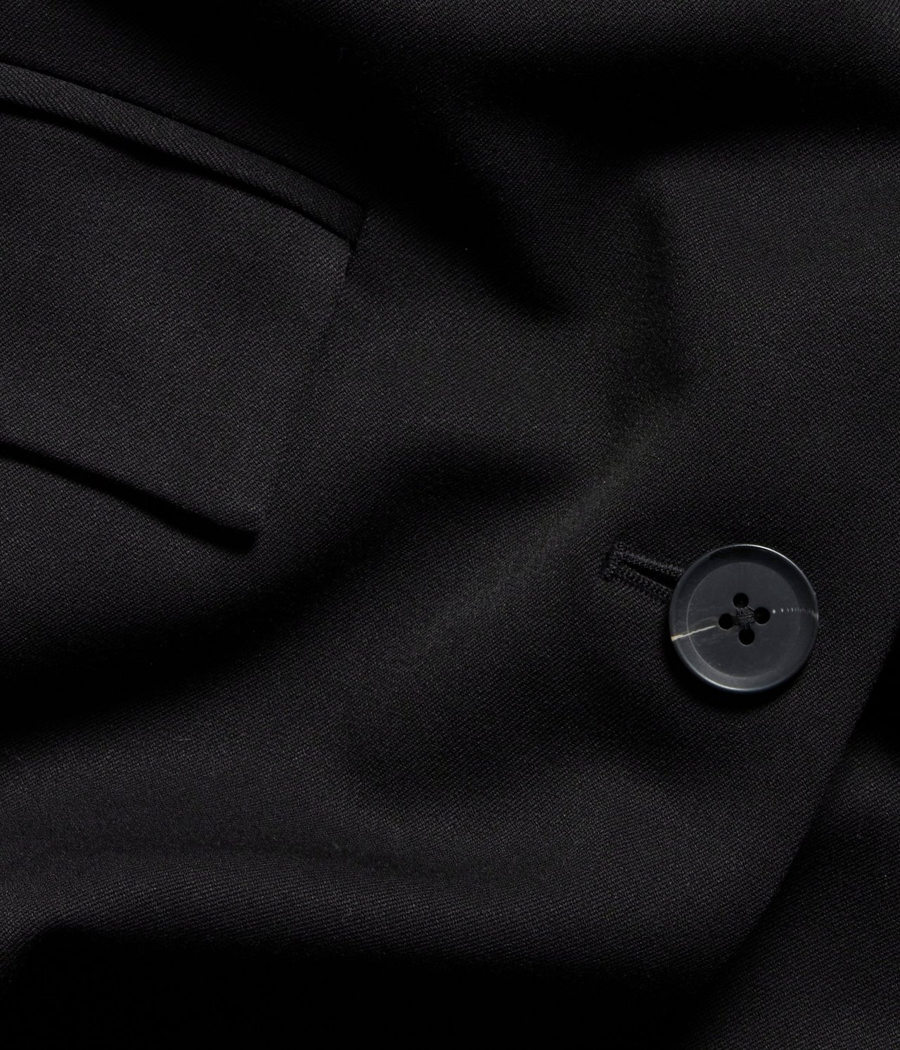 Zbliżenie czarnej marynarki z ciemnym marmurkowym guzikiem i kieszenią z klapką.