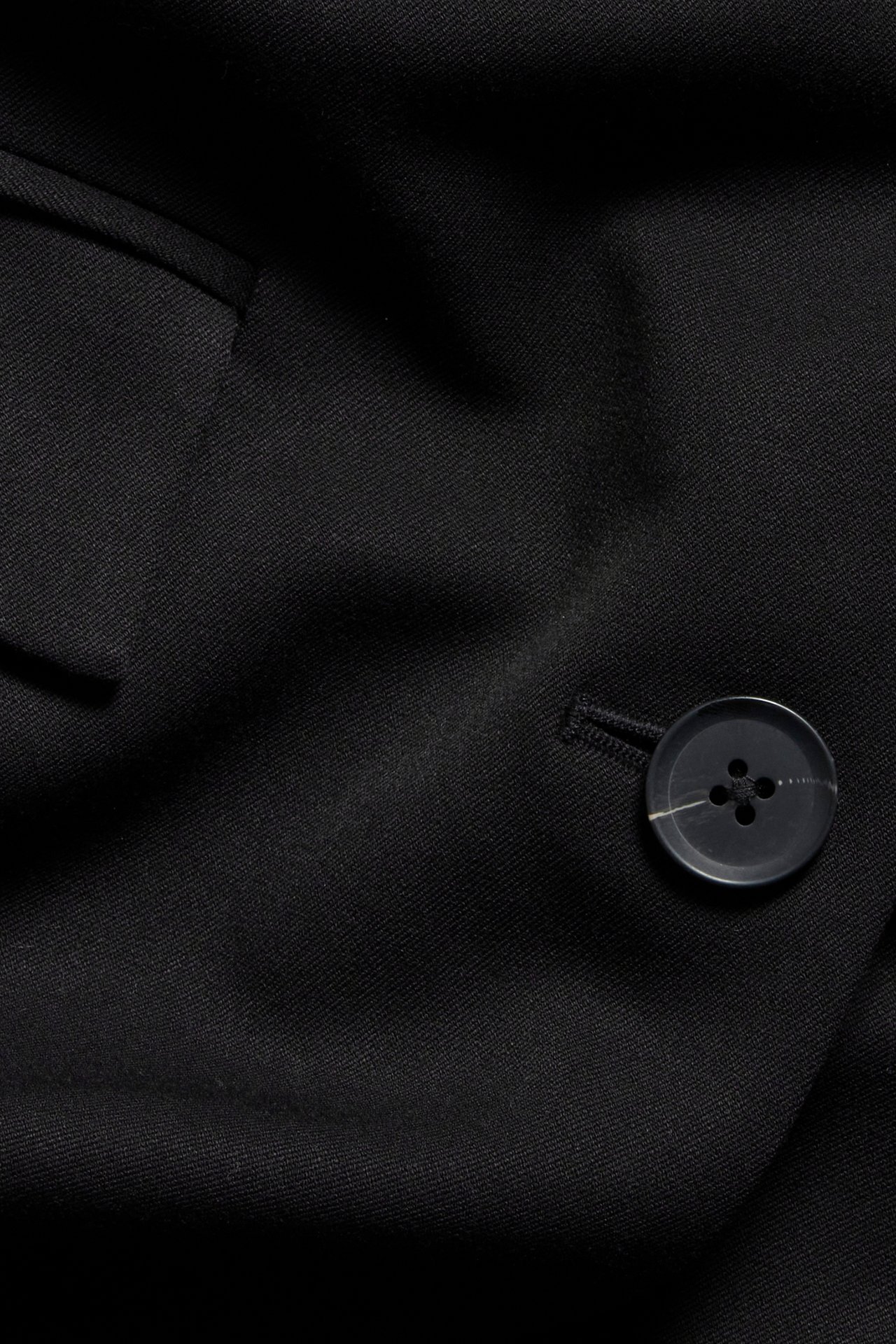 Zbliżenie na czarną marynarkę, widać fakturę materiału i guzik z subtelnym białym paskiem.