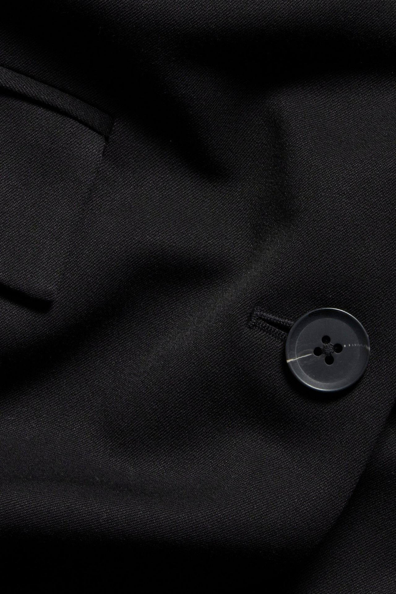 Zbliżenie na czarną marynarkę, widać fakturę materiału i guzik z subtelnym białym paskiem.