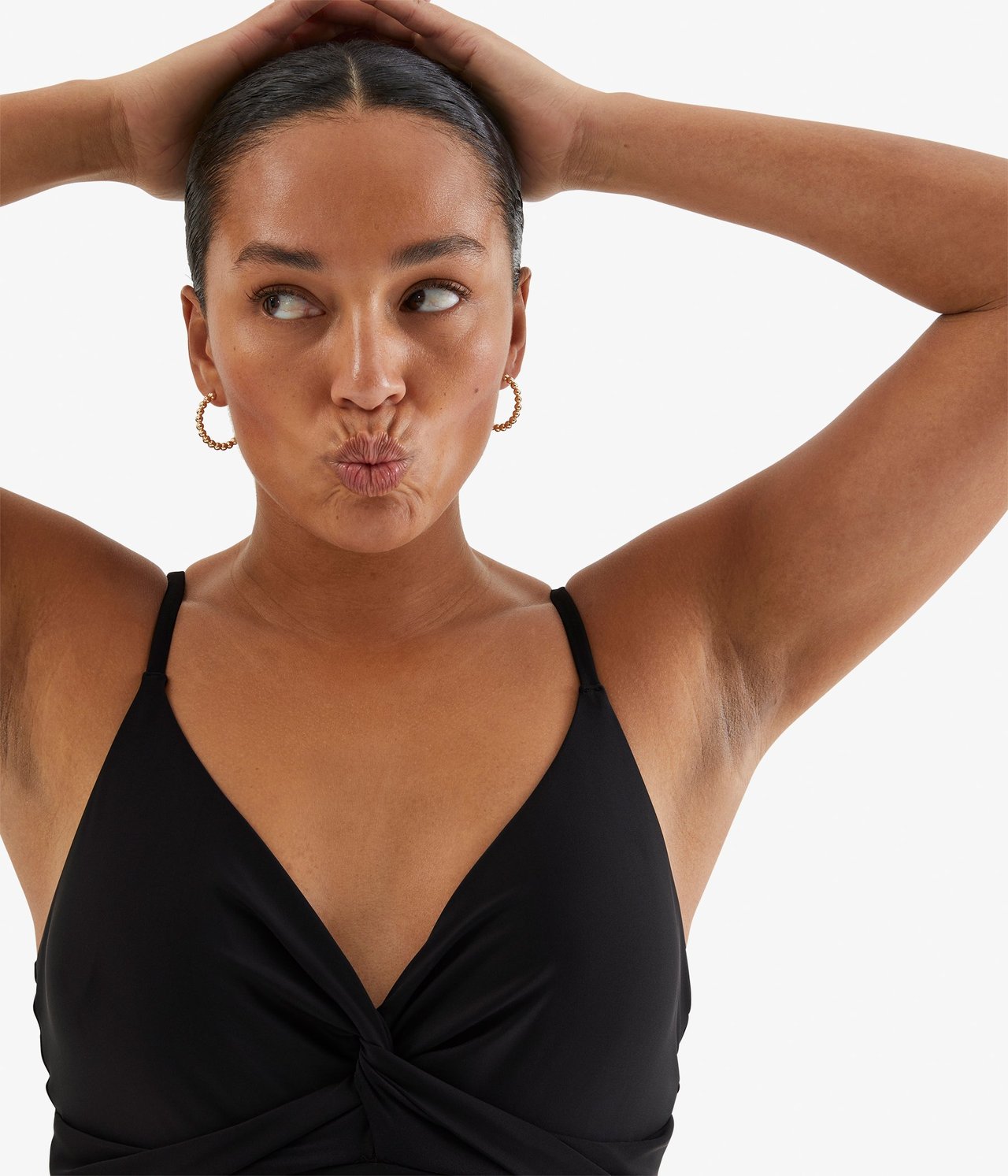 Zbliżenie z przodu kobiety w czarnym kostiumie kąpielowym z drapowaniem i złotymi kolczykami kołami.