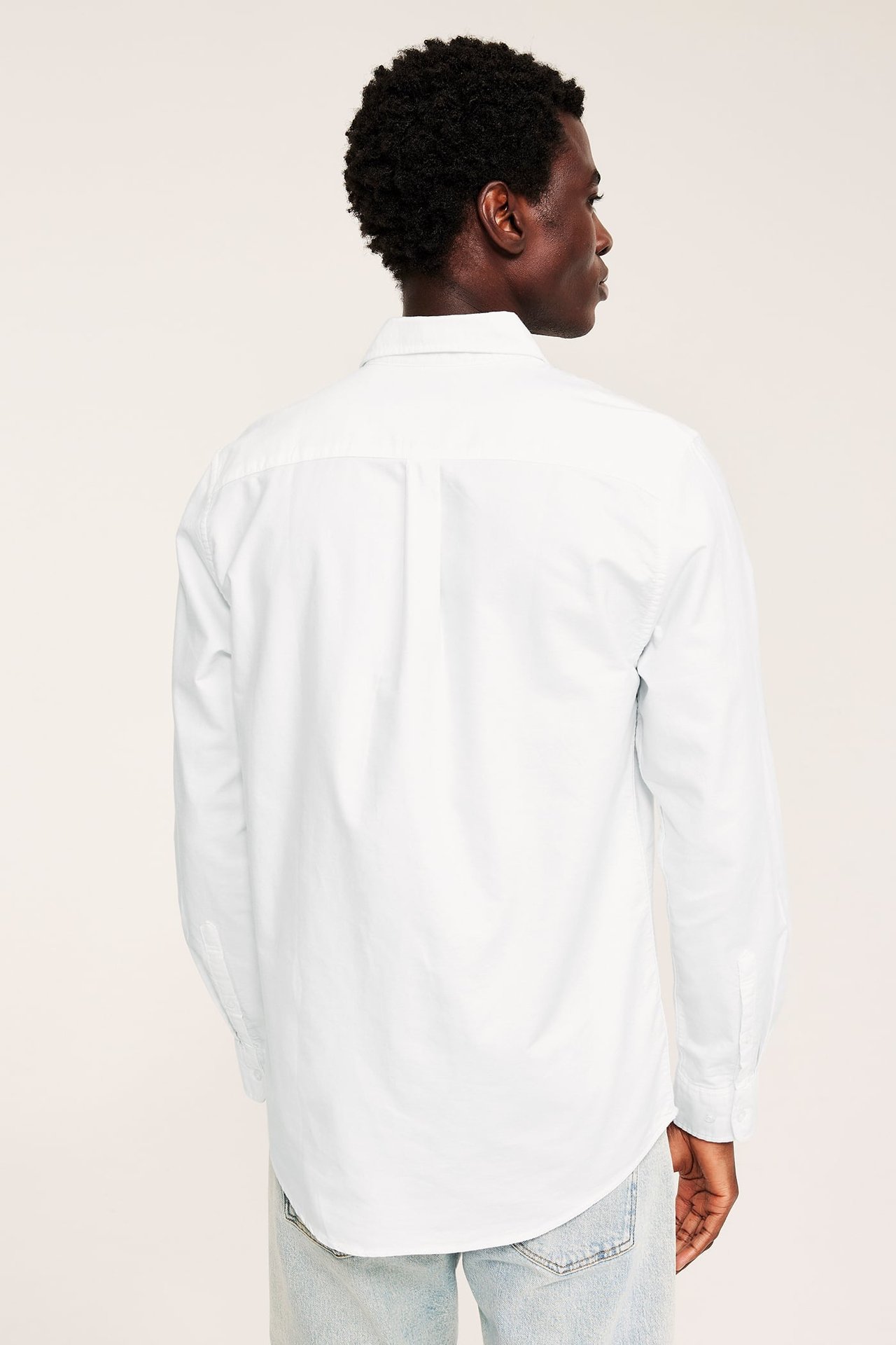 Bakfra av en mann i hvit langermet skjorte og lyseblå jeans.