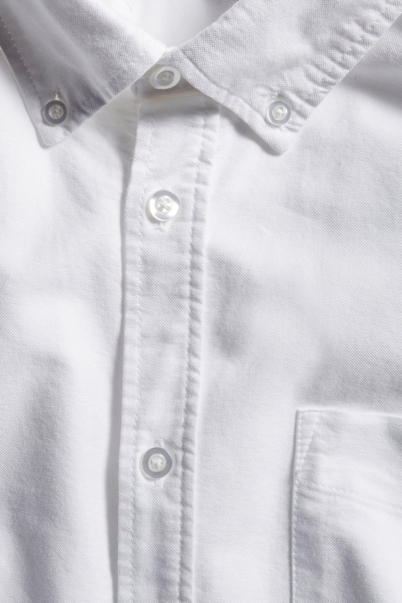 Zbliżenie białej męskiej koszuli oxford o regularnym kroju z kołnierzykiem button-down, listwą guzikową i kieszenią.
