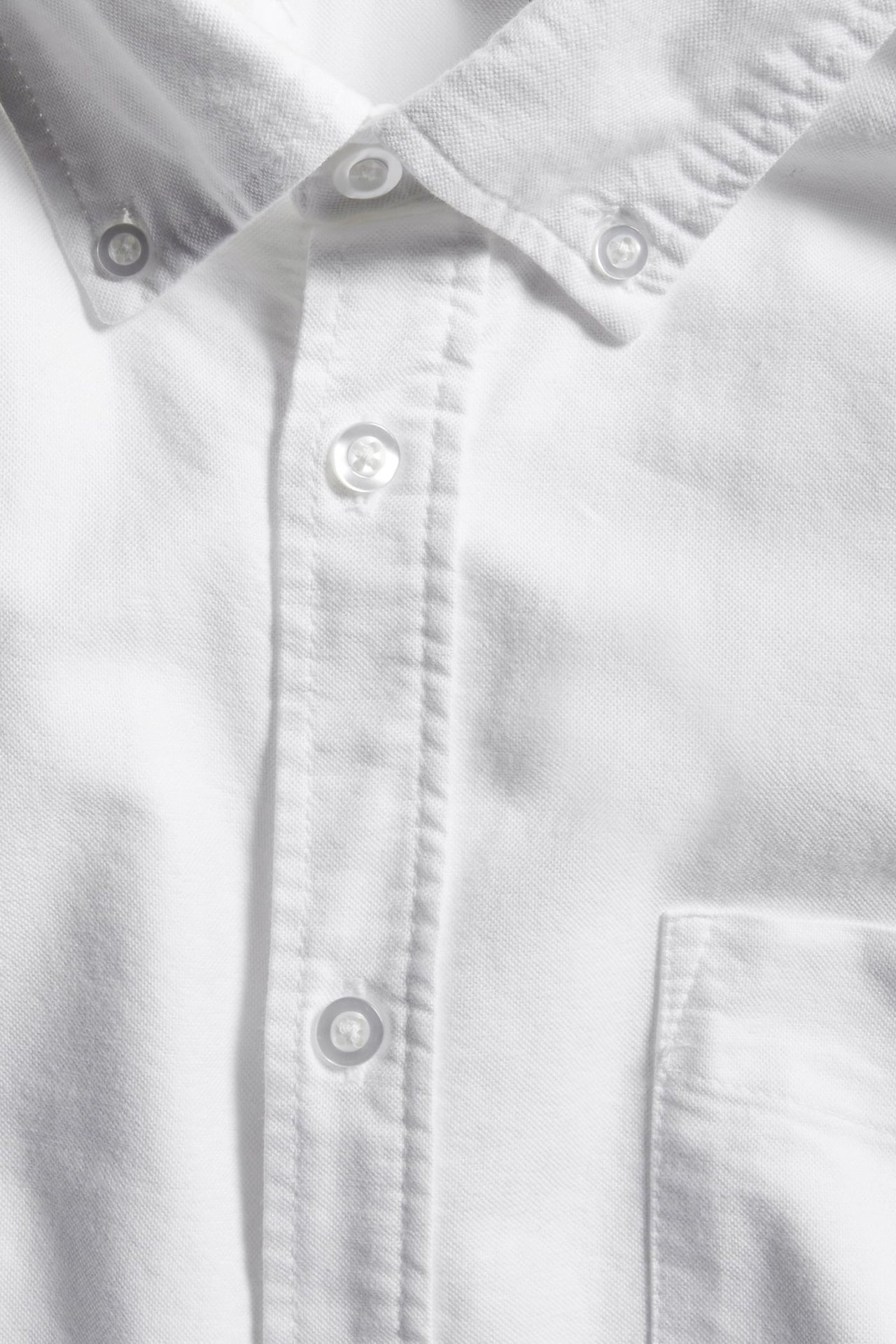 Zbliżenie na męską białą koszulę oxford o regularnym kroju, z kołnierzykiem button-down i kieszenią.